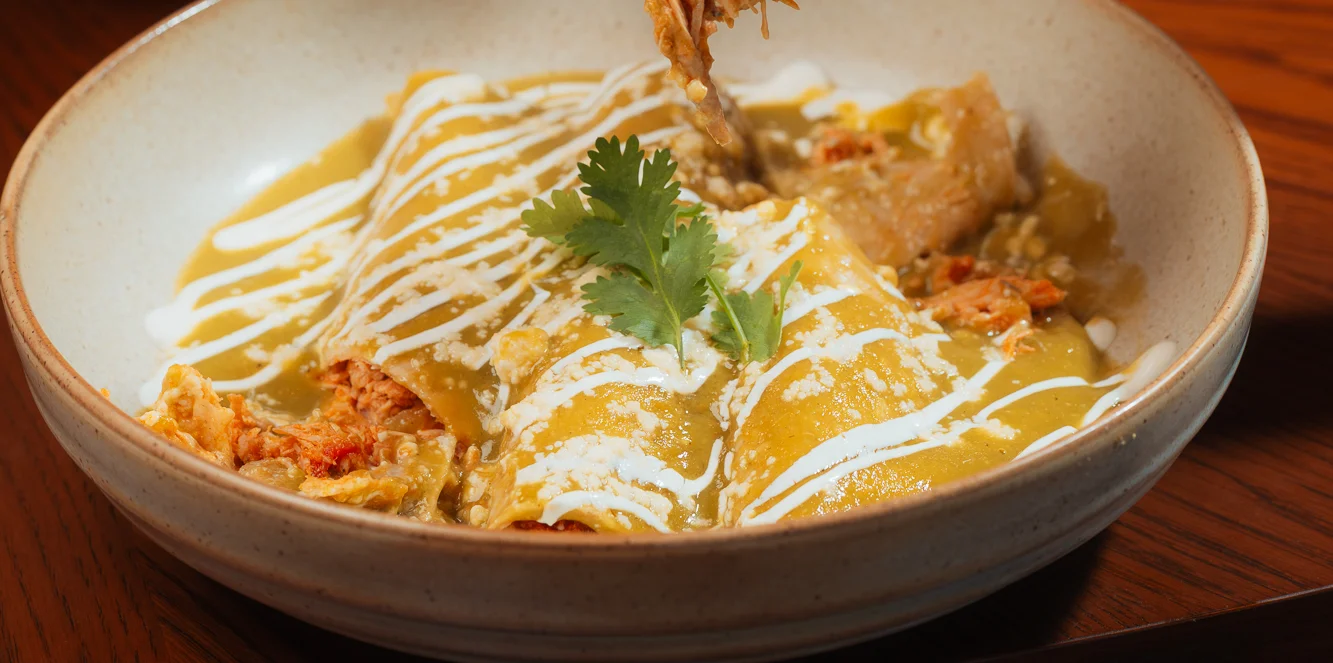 Plate of enchiladas topped with sauce and crema in a restaurant setting