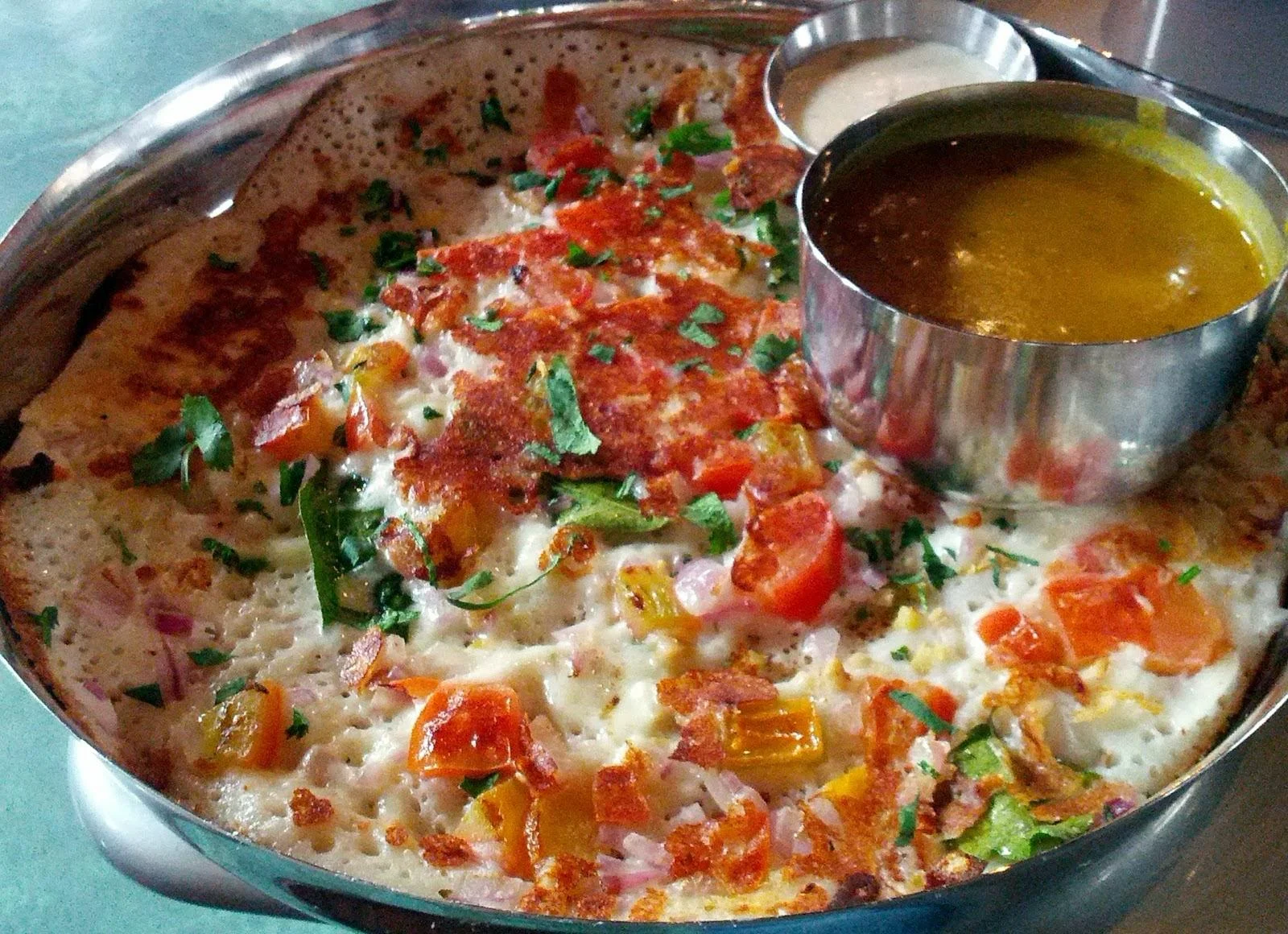A large round crepe filled with vegetables and served with dipping sauces in bowls.