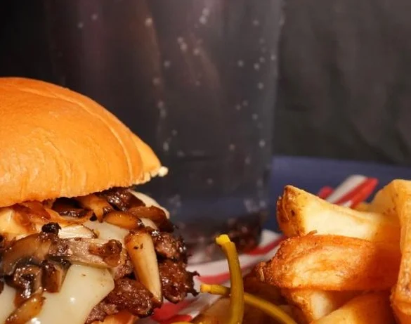A savory burger with melted cheese and sautéed mushrooms, served alongside crispy fries and a dark soda.