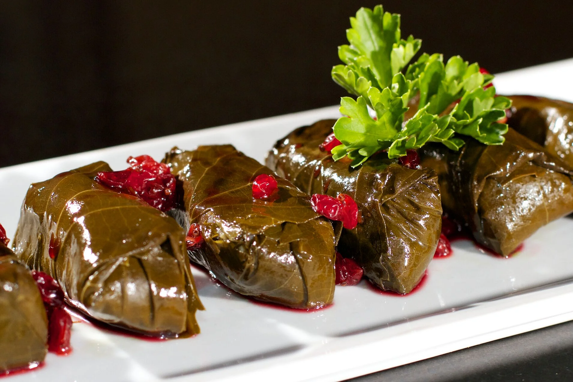 A close-up of stuffed grape leaves drizzled with a sweet sauce and garnished with fresh herbs.