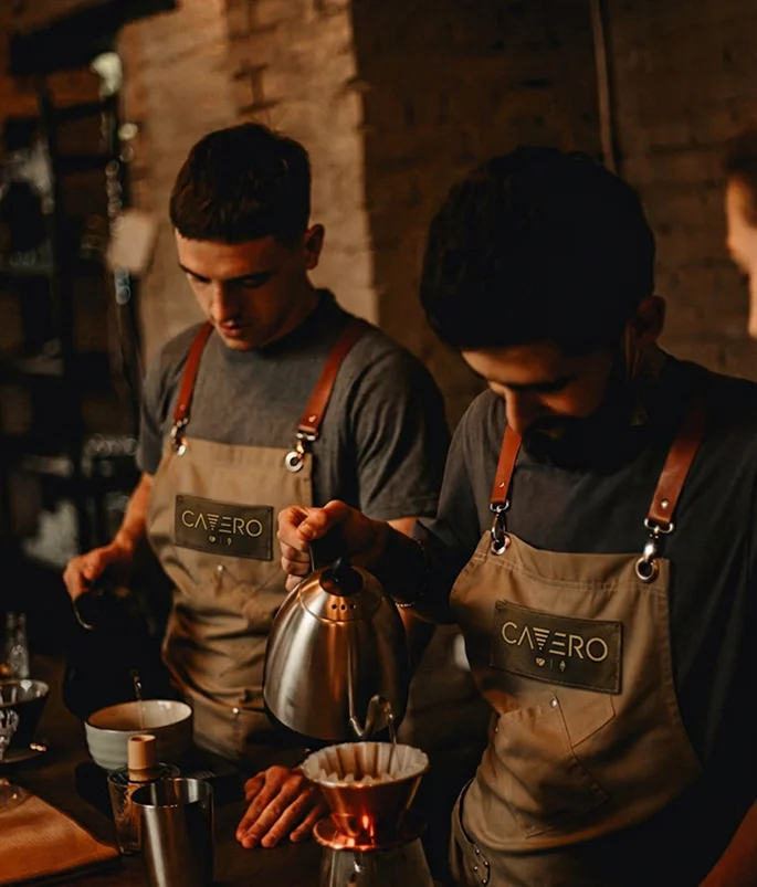 Baristas preparing pour-over coffee in a warm café setting