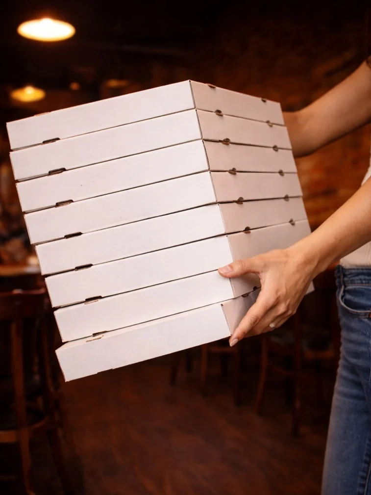 A person holding a tall stack of white pizza boxes, showcasing multiple layers.