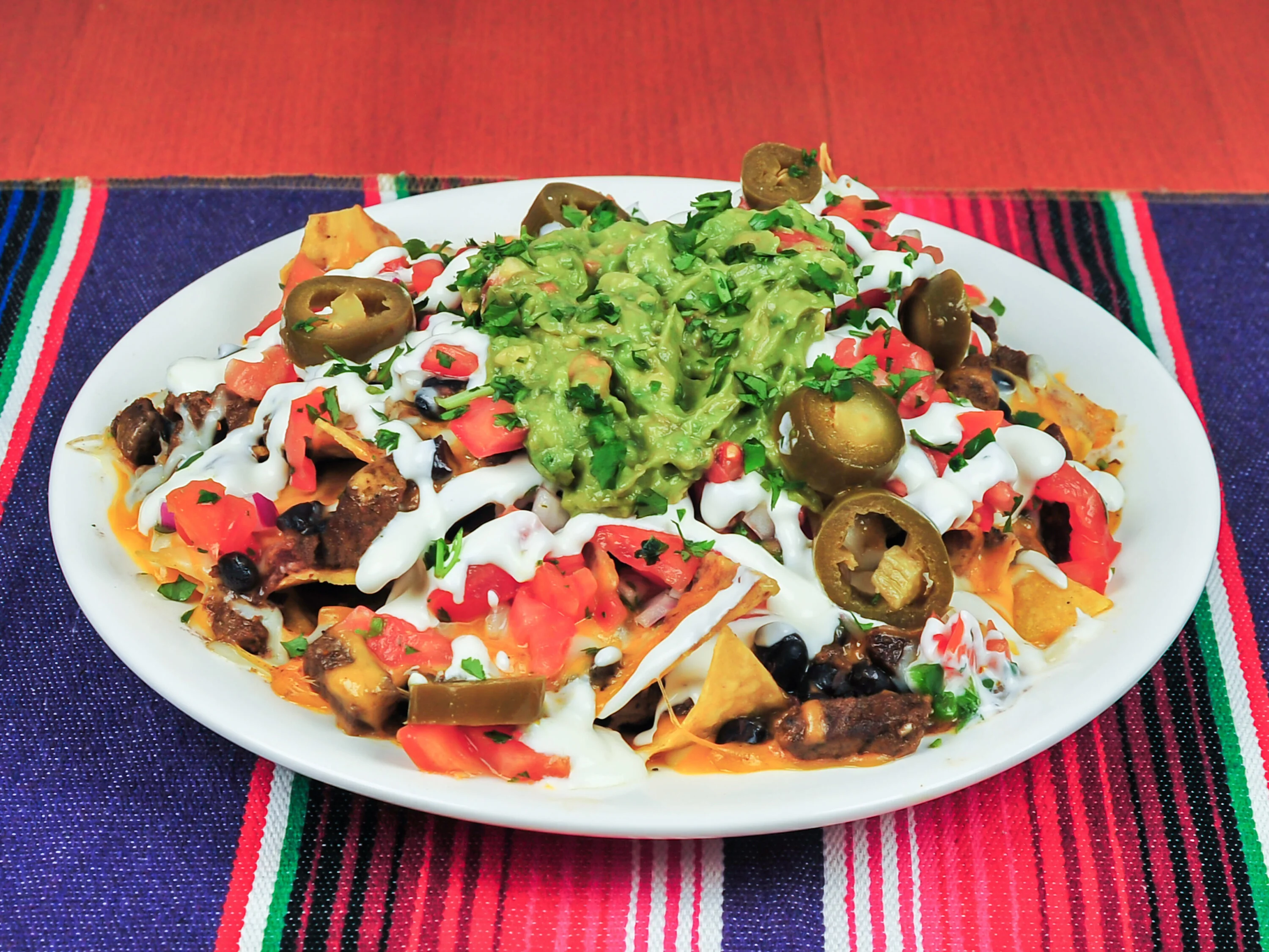A vibrant plate of nachos piled high with toppings including guacamole, diced tomatoes, jalapeños, and sour cream.