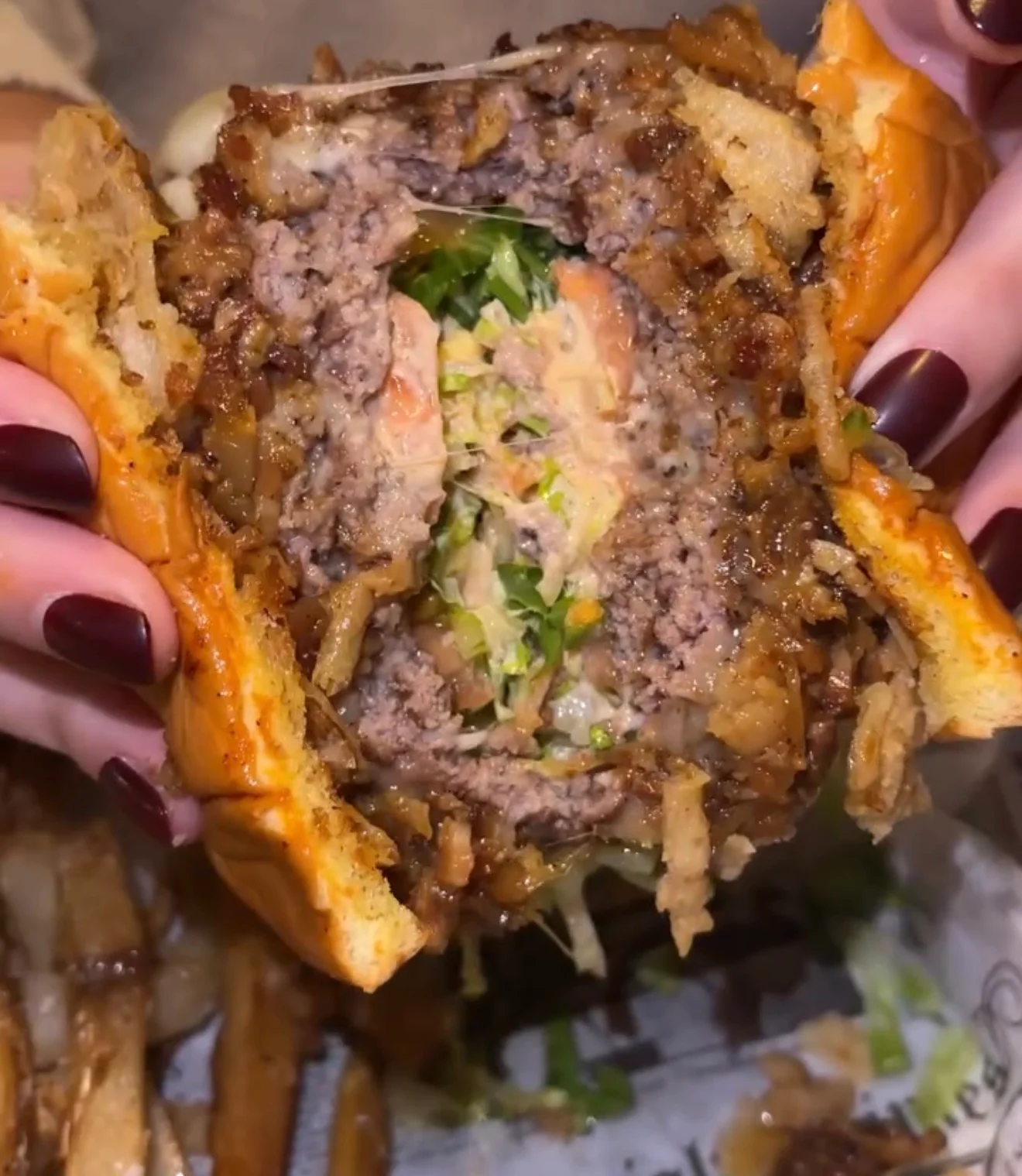 A cross-section of a burger revealing layers of meat, lettuce, and sauce, served with a side of fries.