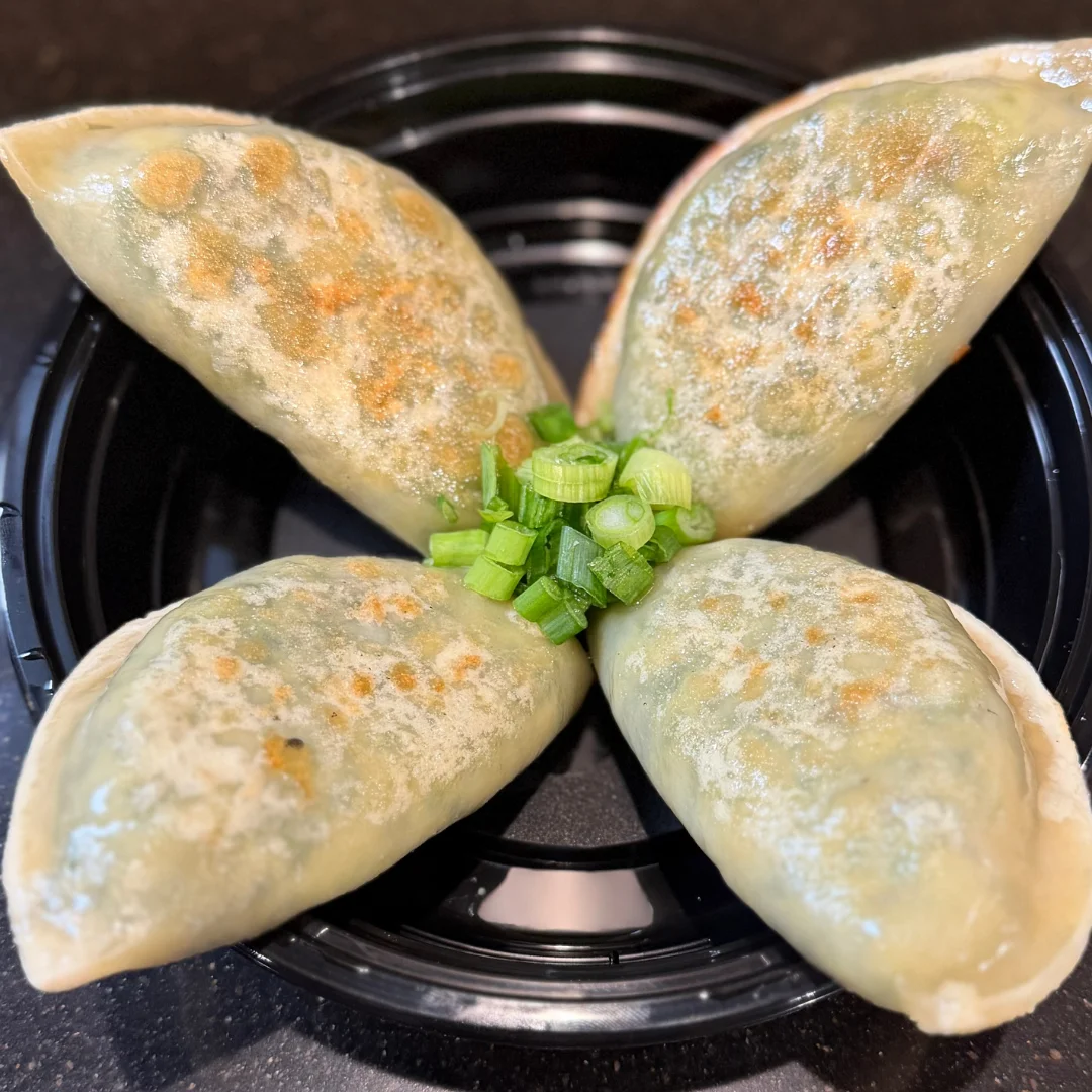 Four golden-brown dumplings arranged in a flower shape with chopped green onions.