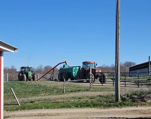 Tractors working on a farm with green fields and blue sky