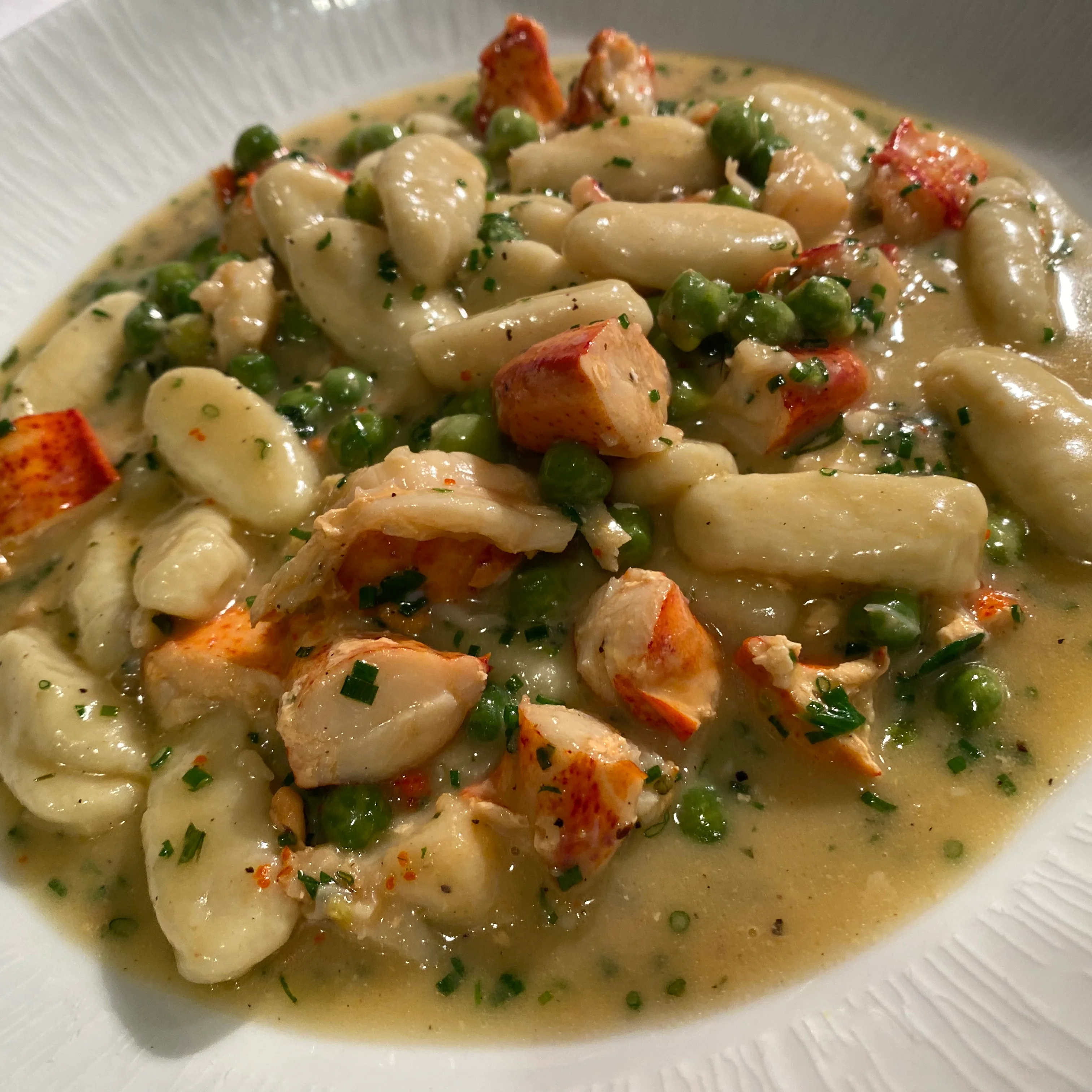 A collection of uncooked pasta pieces scattered on a wooden surface. The pasta is shaped like small shells with a smooth texture.