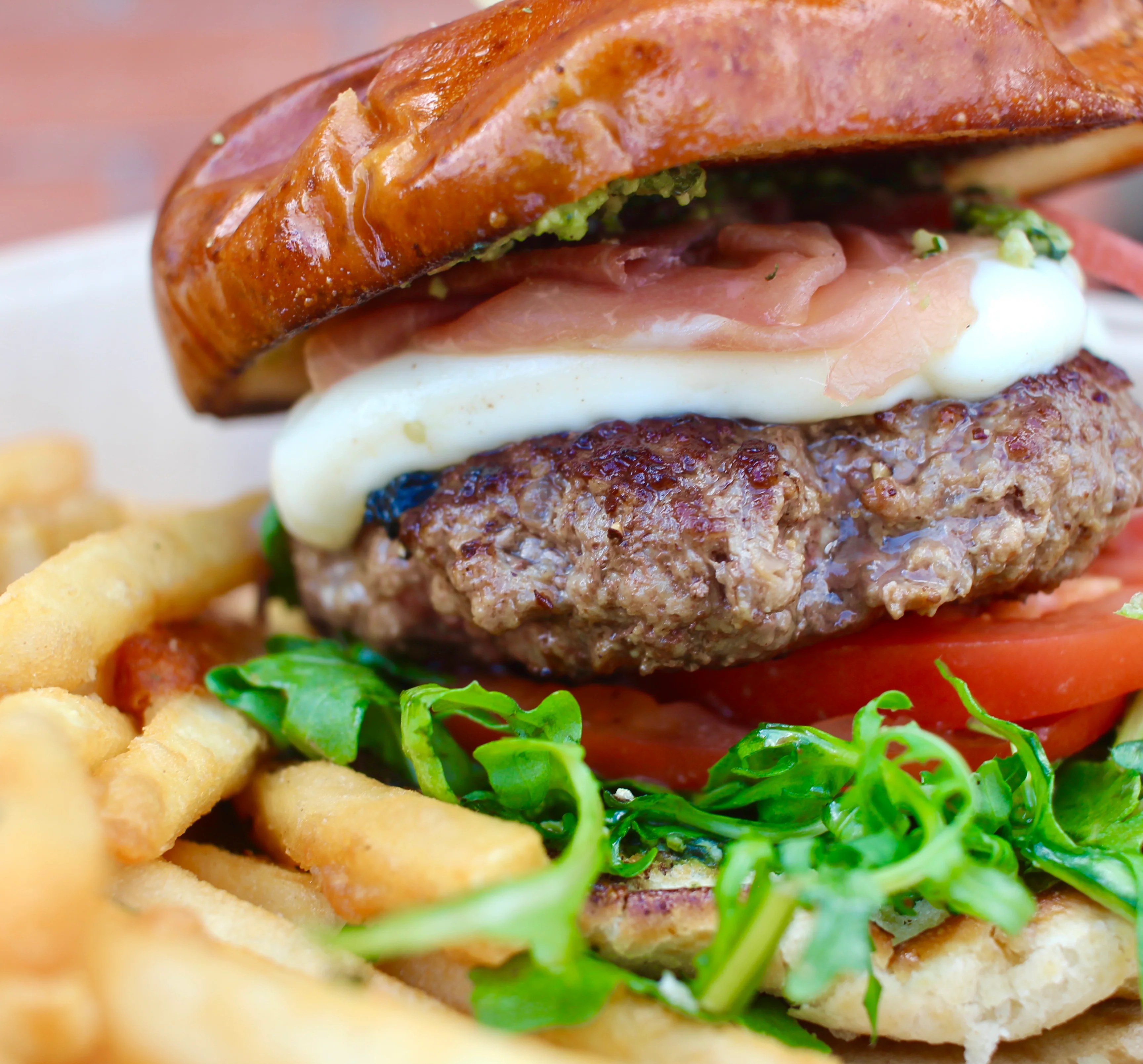 A mouthwatering burger featuring a juicy patty, fresh lettuce, tomato slices, and toppings, all nestled in a shiny pretzel bun.
