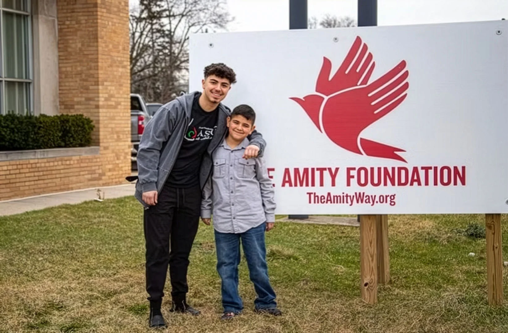 Two boys smiling in front of the Amity Foundation sign