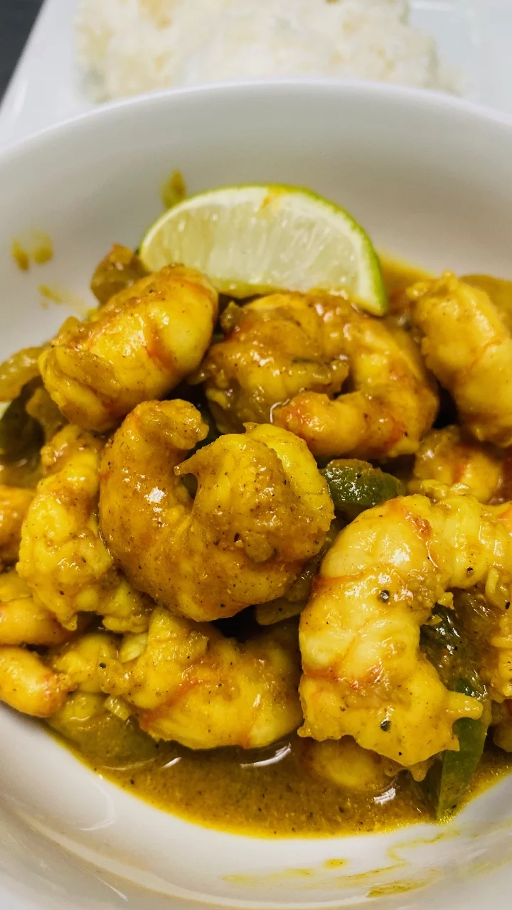 A vibrant dish of shrimp cooked in a seasoned sauce, garnished with a lime wedge, served with a side of rice.