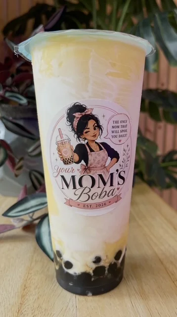 A creamy boba drink with a gradient of yellow and white, revealing black tapioca pearls at the bottom. The cup showcases a charming logo.