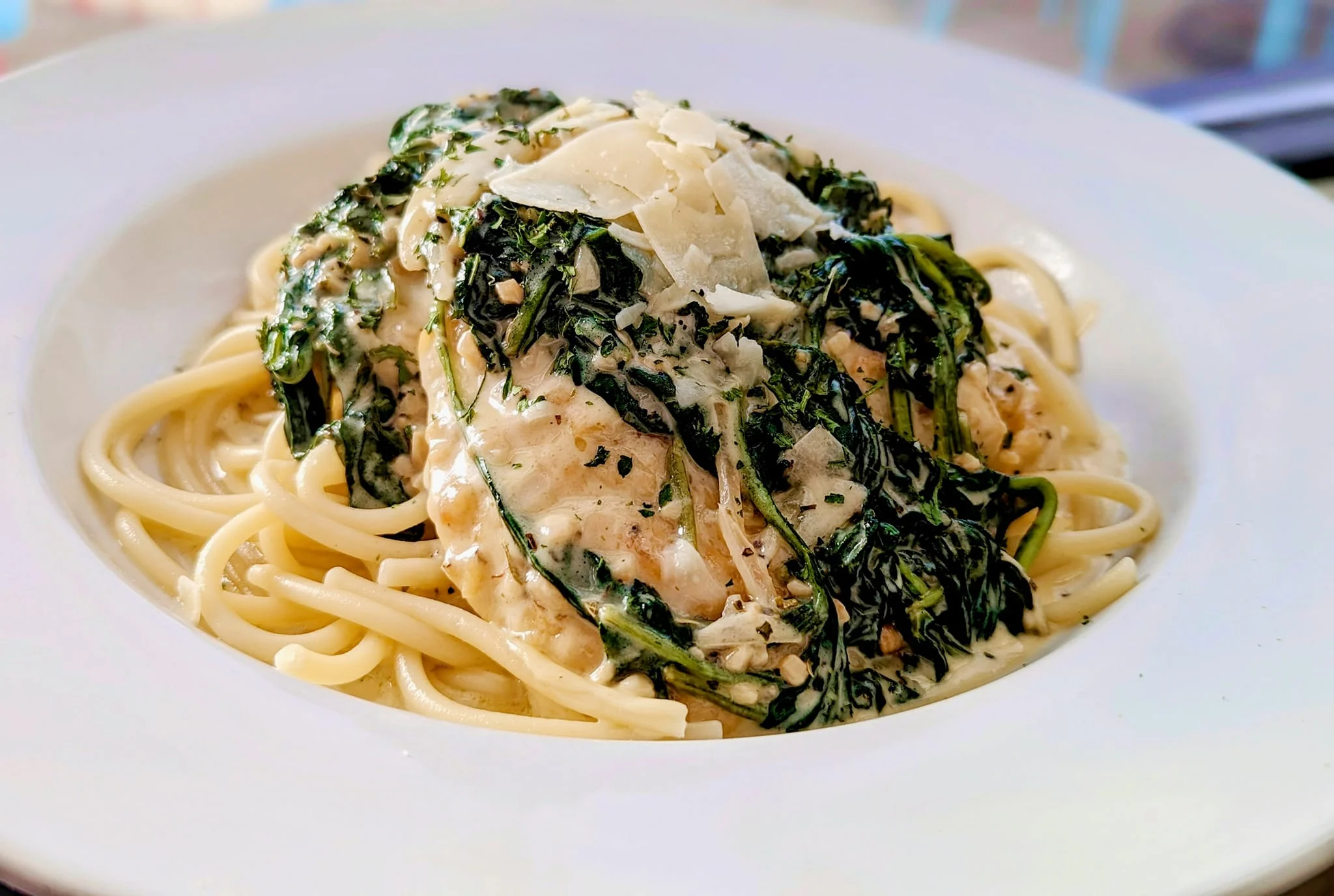 A plate of linguine topped with creamy sauce, spinach, and grated cheese.