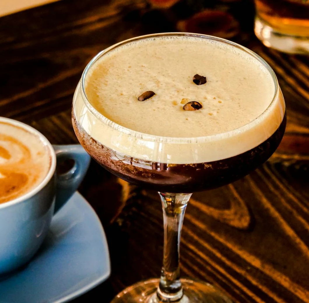 A cocktail with coffee beans beside a latte and a dessert on a wooden table.