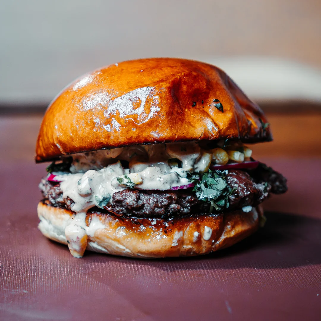 A gourmet burger showcasing a juicy patty with toppings and a glossy brioche bun.