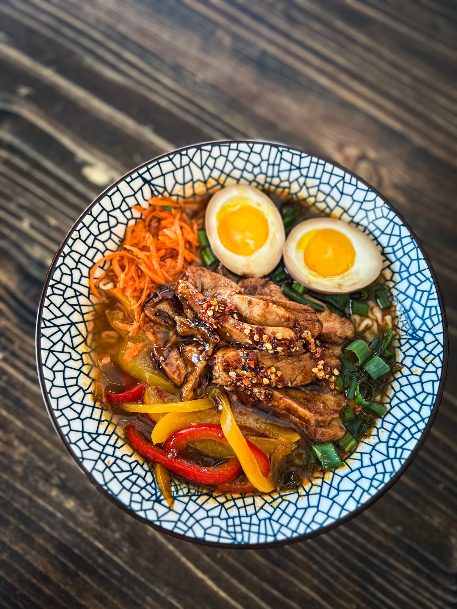 Bowl of ramen with sliced meat, soft-boiled eggs, and colorful vegetables.