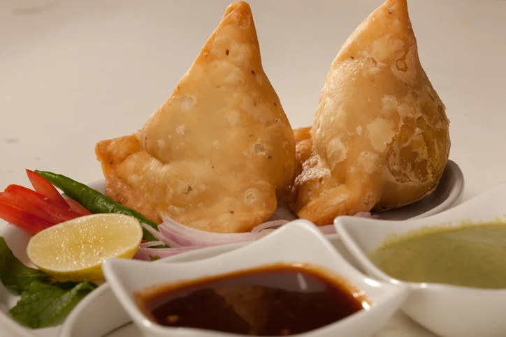 Crispy Indian samosas served with chutneys and fresh garnishes
