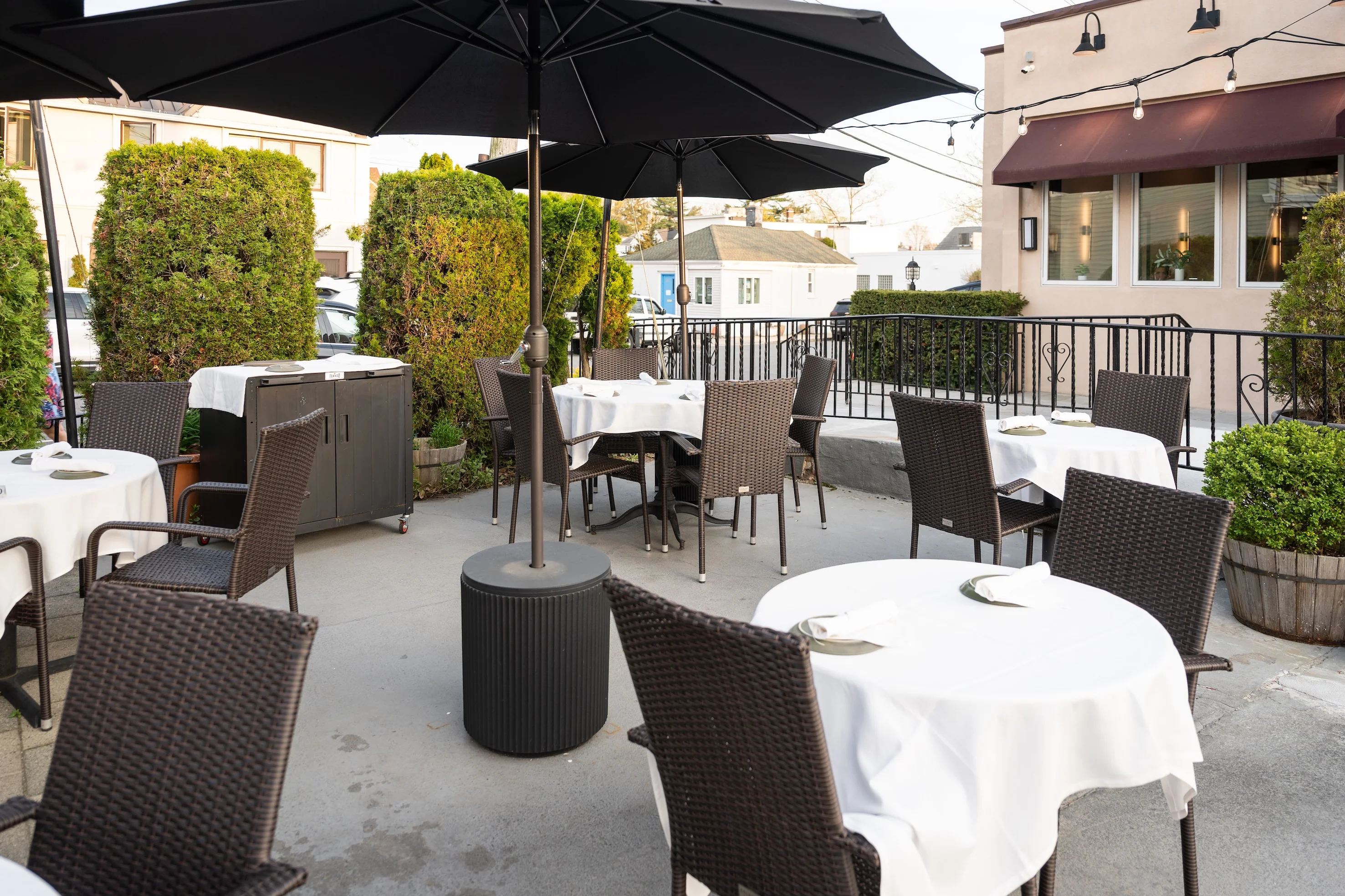 Toscana on Main outdoor dining area with tables, chairs, and umbrellas surrounded by greenery, creating a cozy atmosphere for guests.