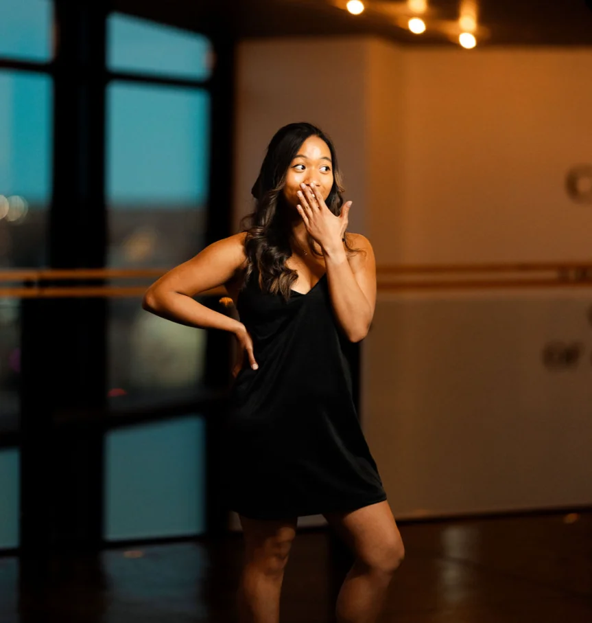 Woman in a black dress posing playfully indoors