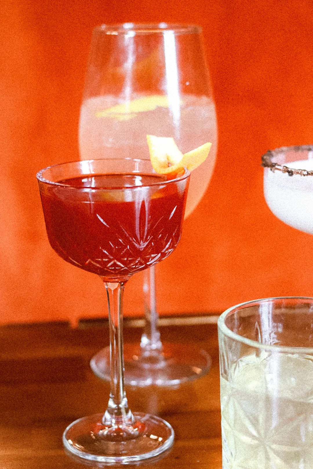 Three colorful cocktails on a wooden table with an orange background.