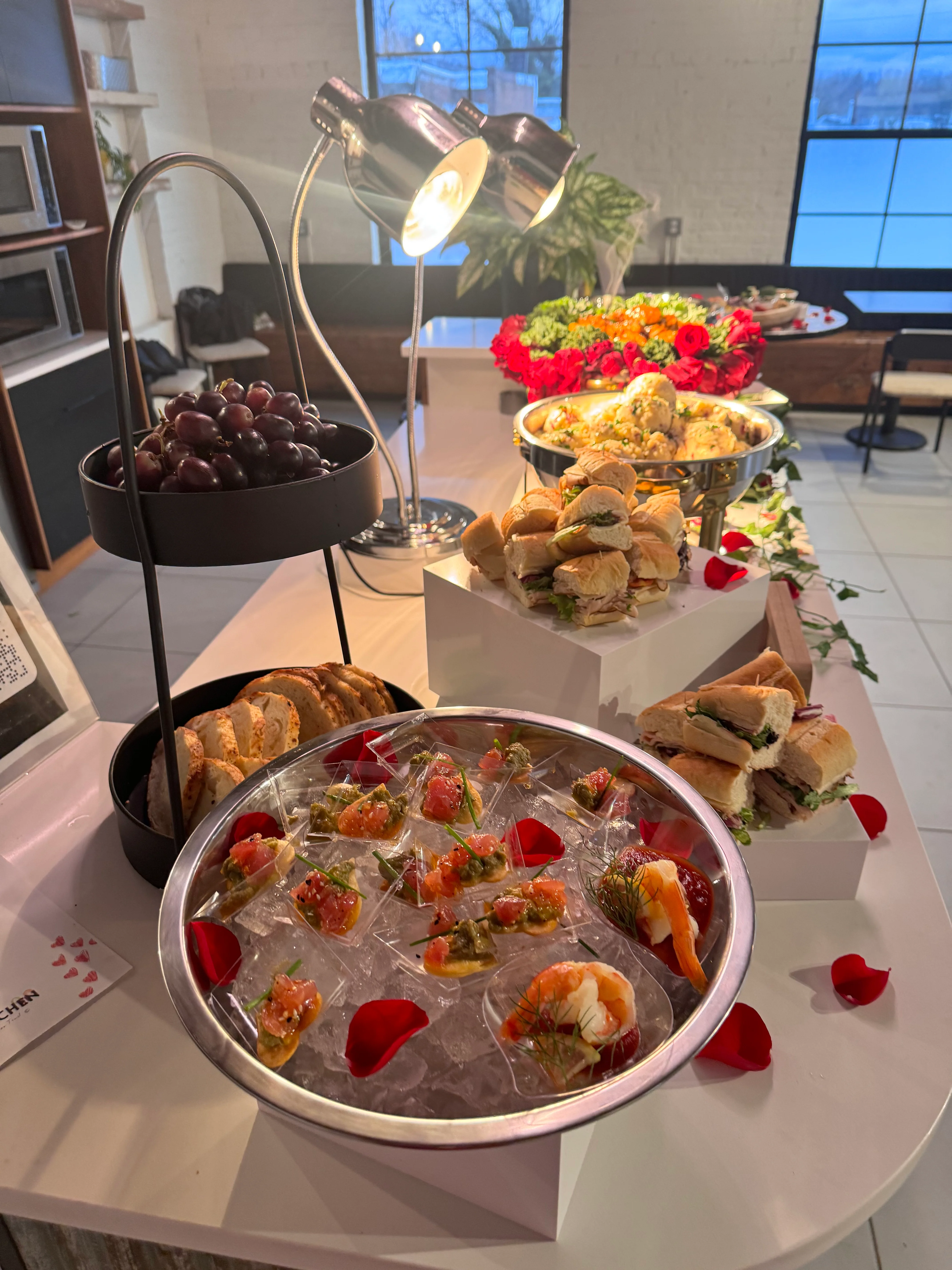 A beautifully arranged spread of appetizers including grapes, sandwiches, and seafood on a table decorated with flowers.