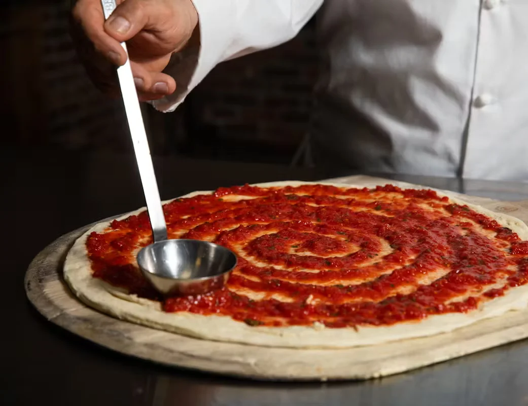 A chef delicately putting tomato sauce on pizza dough