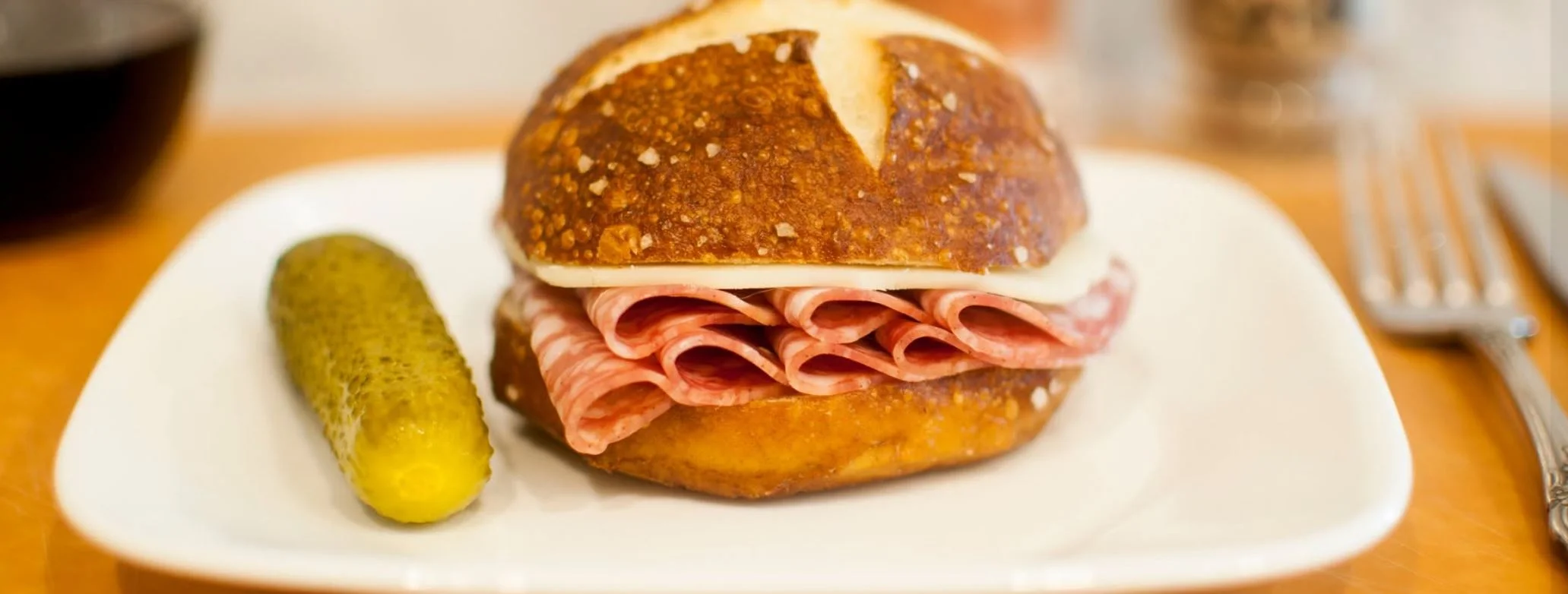 Italian deli sandwich on pretzel bread with salami and pickle