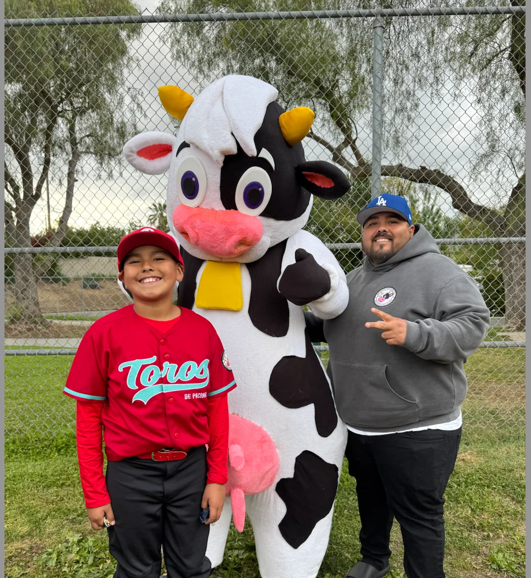 Child in baseball uniform with a cow mascot at a sports event
