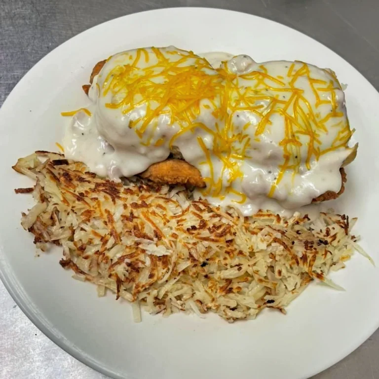 A plate of Eggs Benedict with poached eggs, creamy hollandaise sauce, and melted cheddar cheese on top, accompanied by a side of crispy hashbrowns.