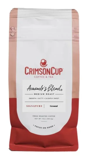 A close-up of a coffee cup with a logo, set on a counter beside a barista working in the background.