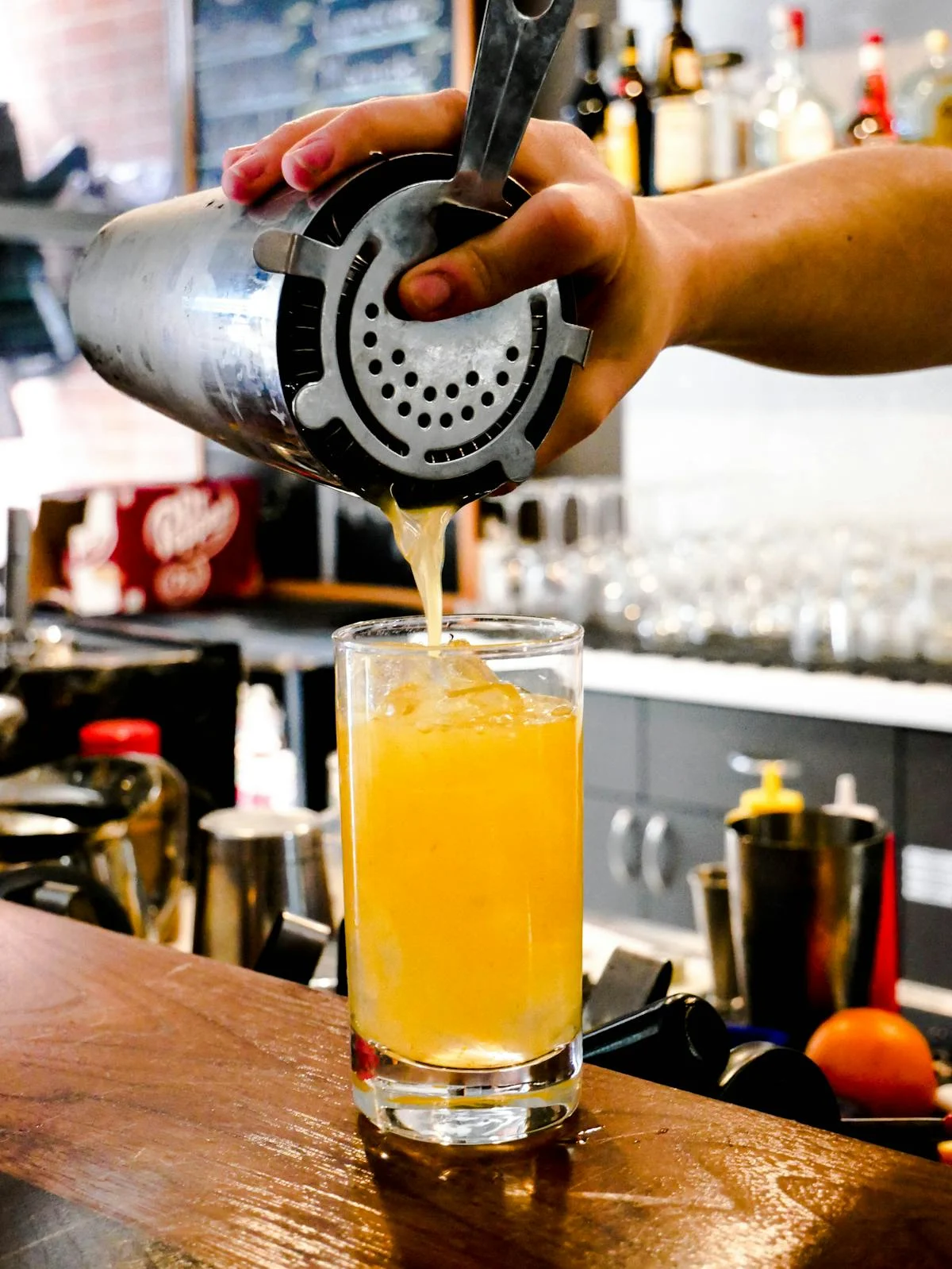 Bartender pouring a yellow cocktail into a glass with ice.