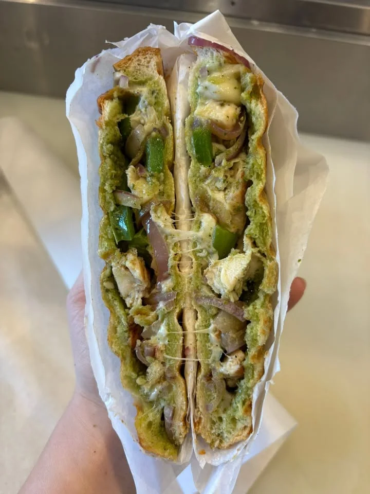 A cross-section of a sandwich filled with cheese, chicken, and green peppers, showcasing its gooey texture.
