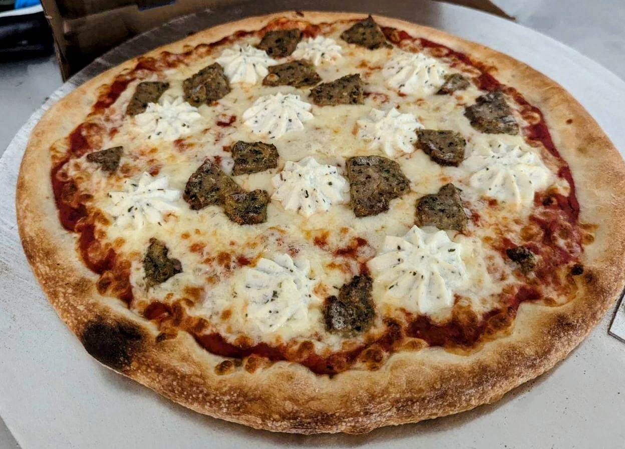 A pizza topped with pieces of meat and dollops of cheese on a golden crust, presented on a round plate.