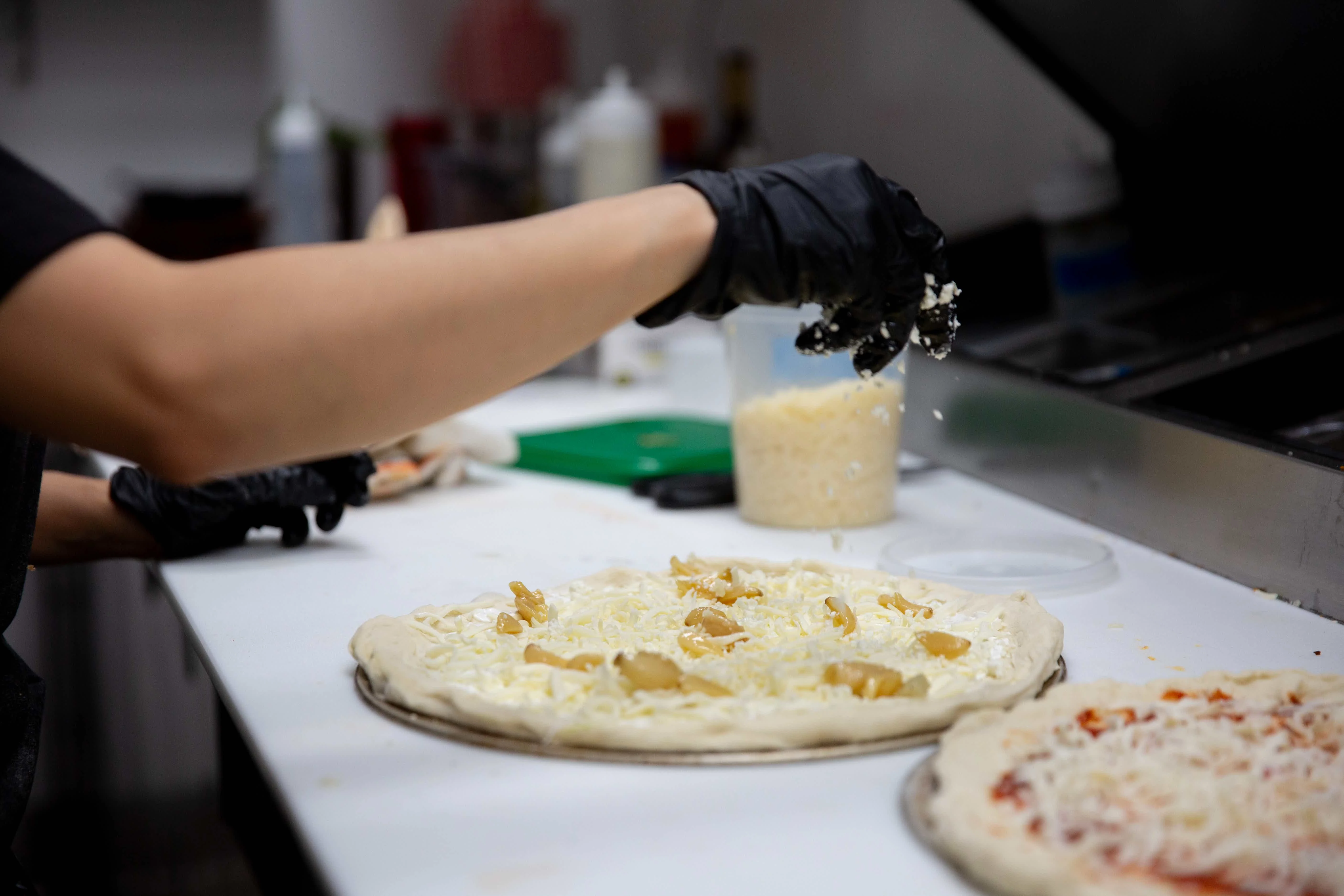 Pizza preparation with cheese and toppings in a restaurant kitchen