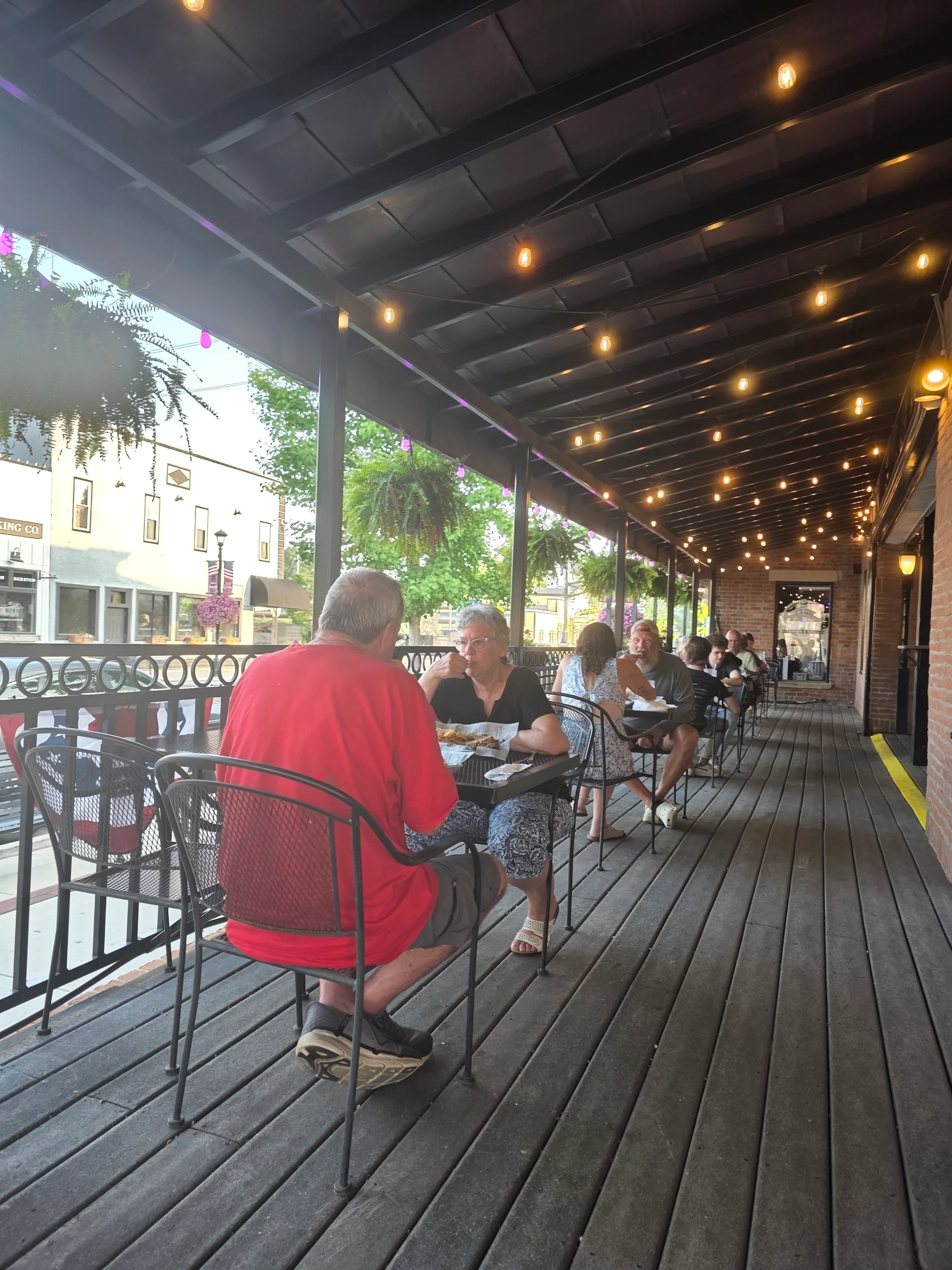 A lively outdoor dining area with patrons enjoying their meals under decorative lights.