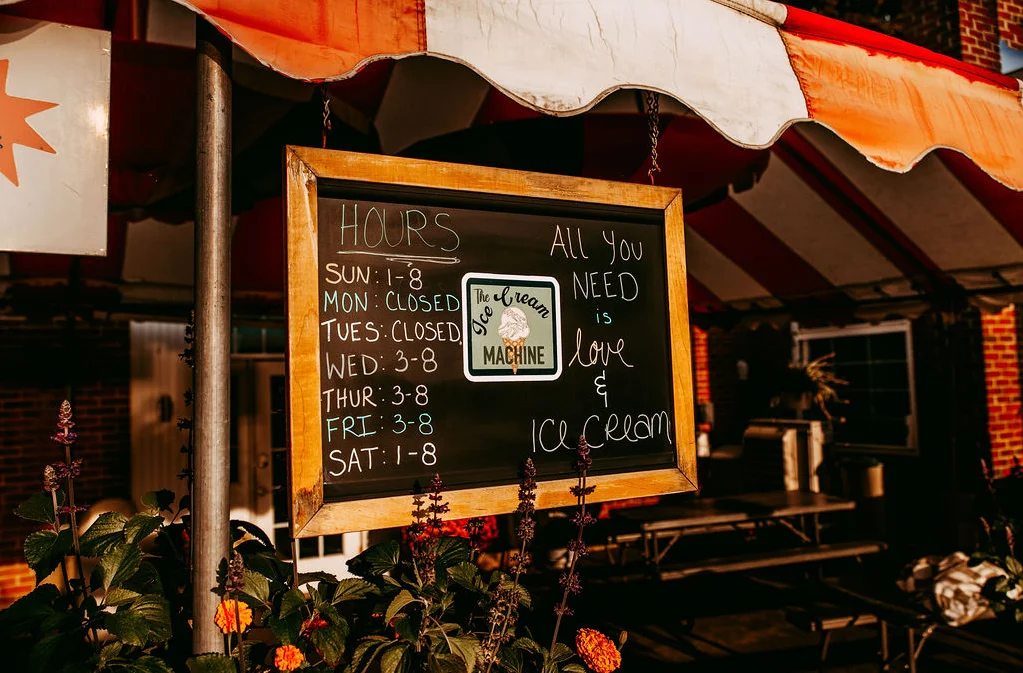Chalkboard menu displaying ice cream shop hours and a love quote