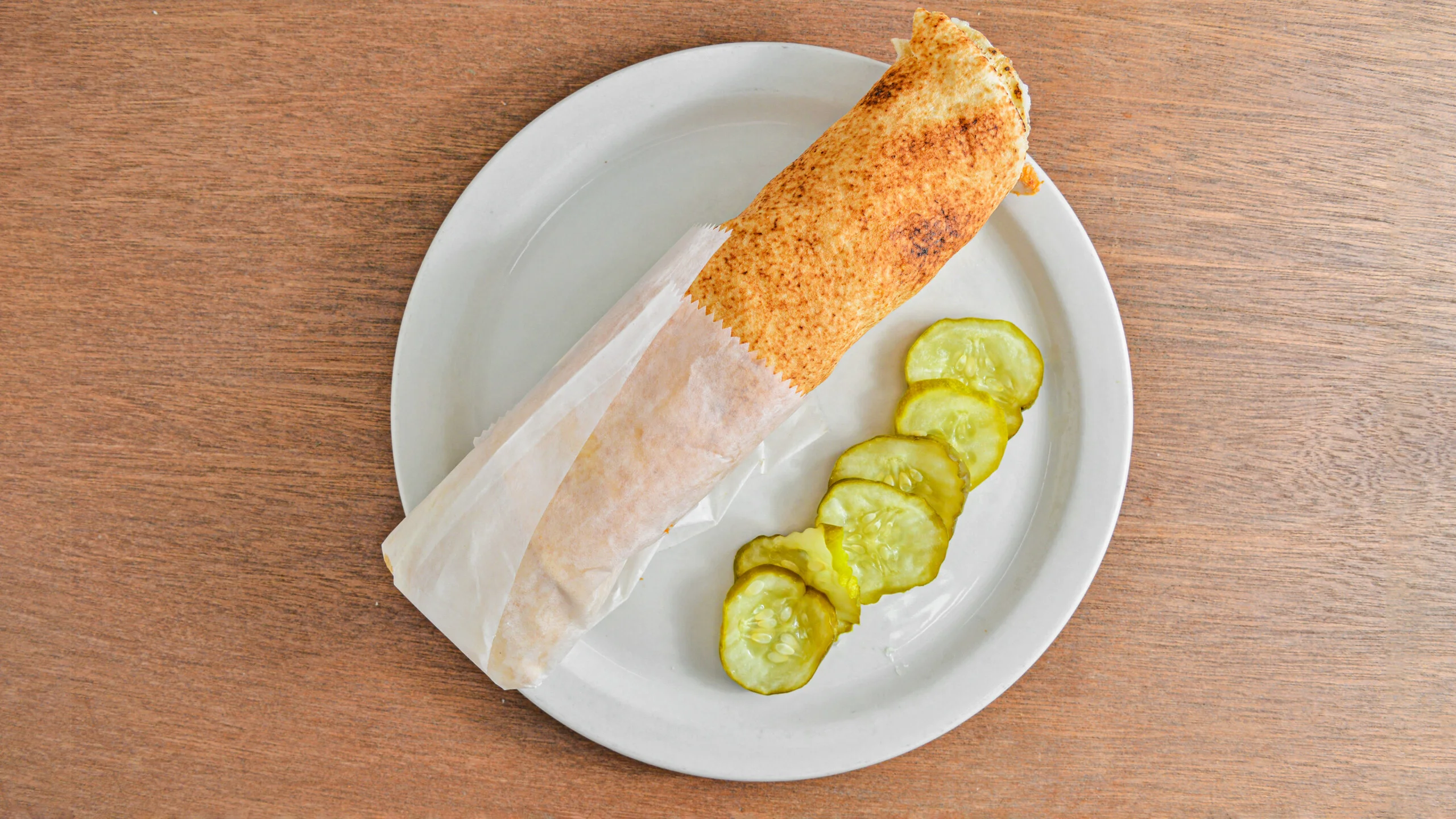 Crispy falafel wrap served with pickles on a white plate