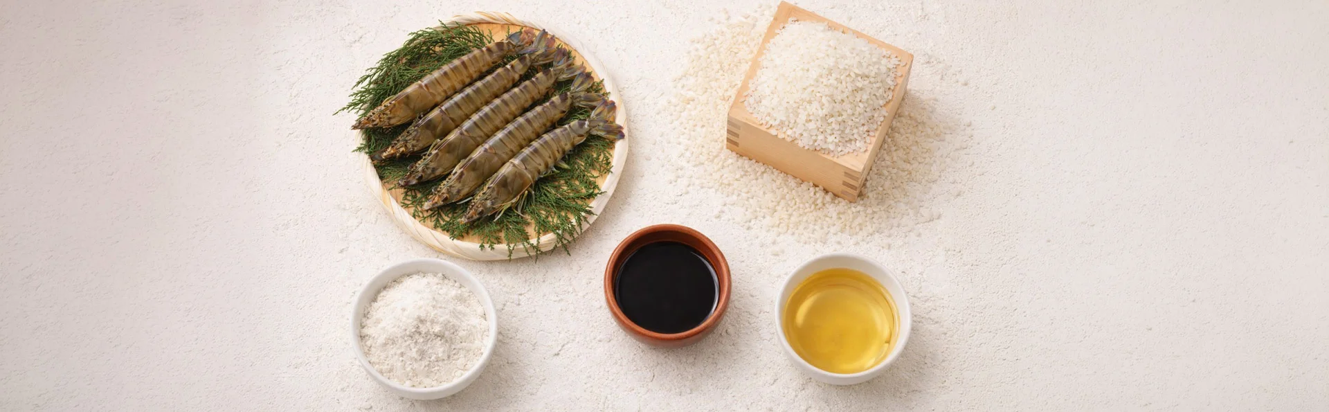 A top-down view showcasing the high-quality ingredients used in Tendon Kohaku's recipes. The different ingredients include rice, sauce and oil in a container, batter in a bowl, and fresh shrimp placed in another bowl.