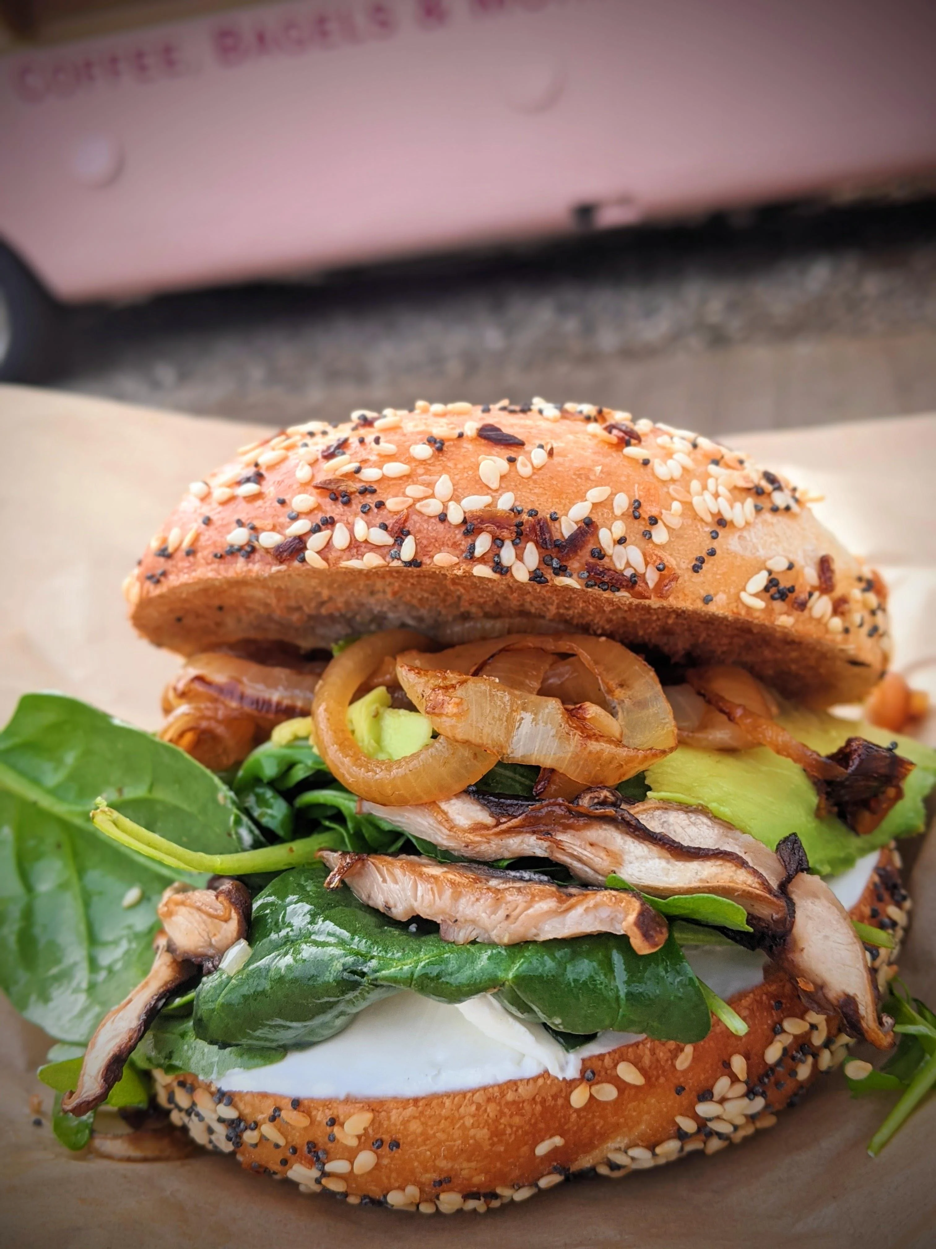 A sesame seed bagel filled with spinach, sautéed mushrooms, and onions, showcasing a fresh and colorful arrangement.