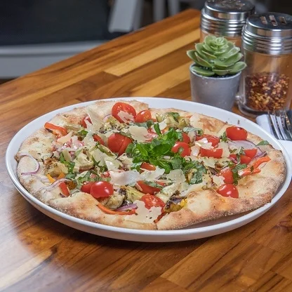 A delicious pizza topped with cherry tomatoes, vegetables, and herbs, served on a wooden table.