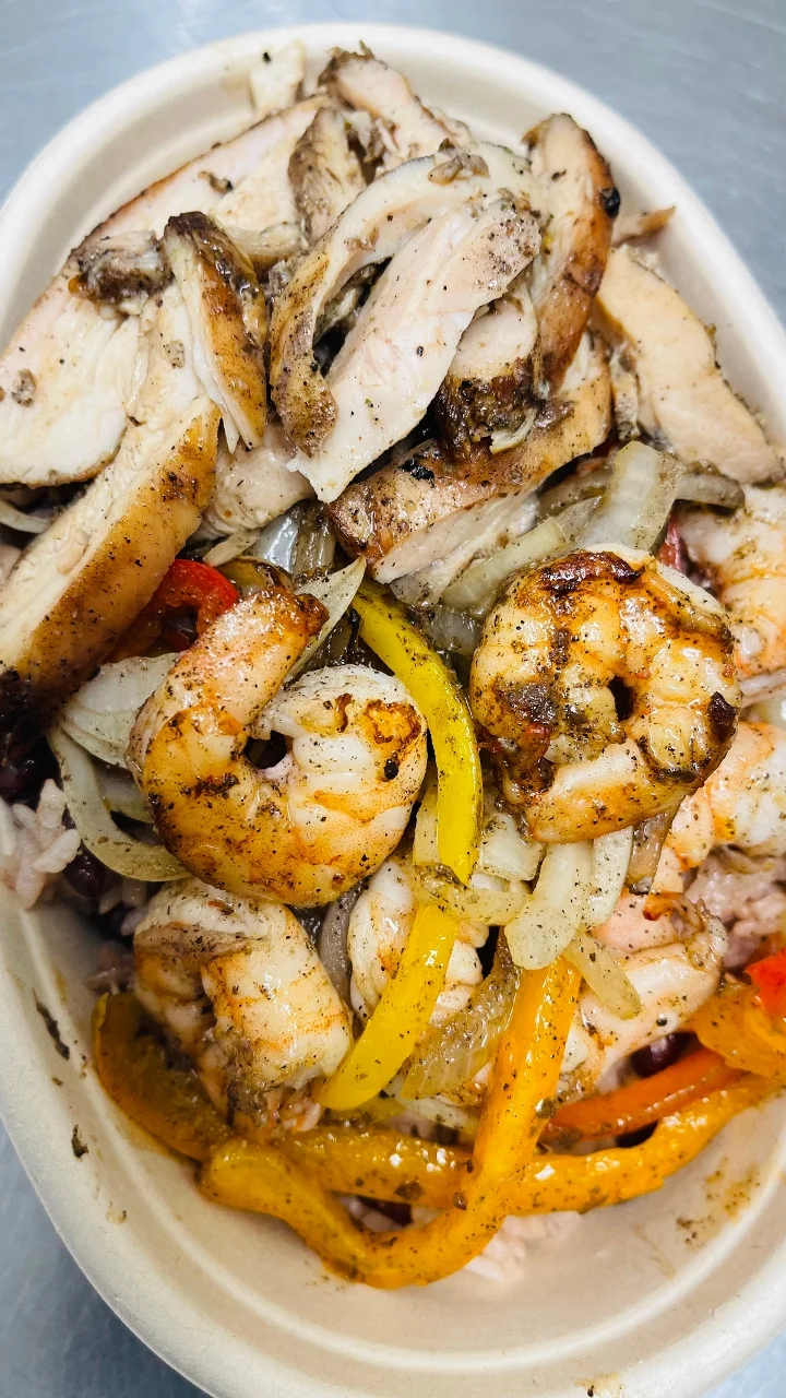 A dish featuring grilled chicken and shrimp, served over a bed of rice with sautéed onions and colorful bell peppers.