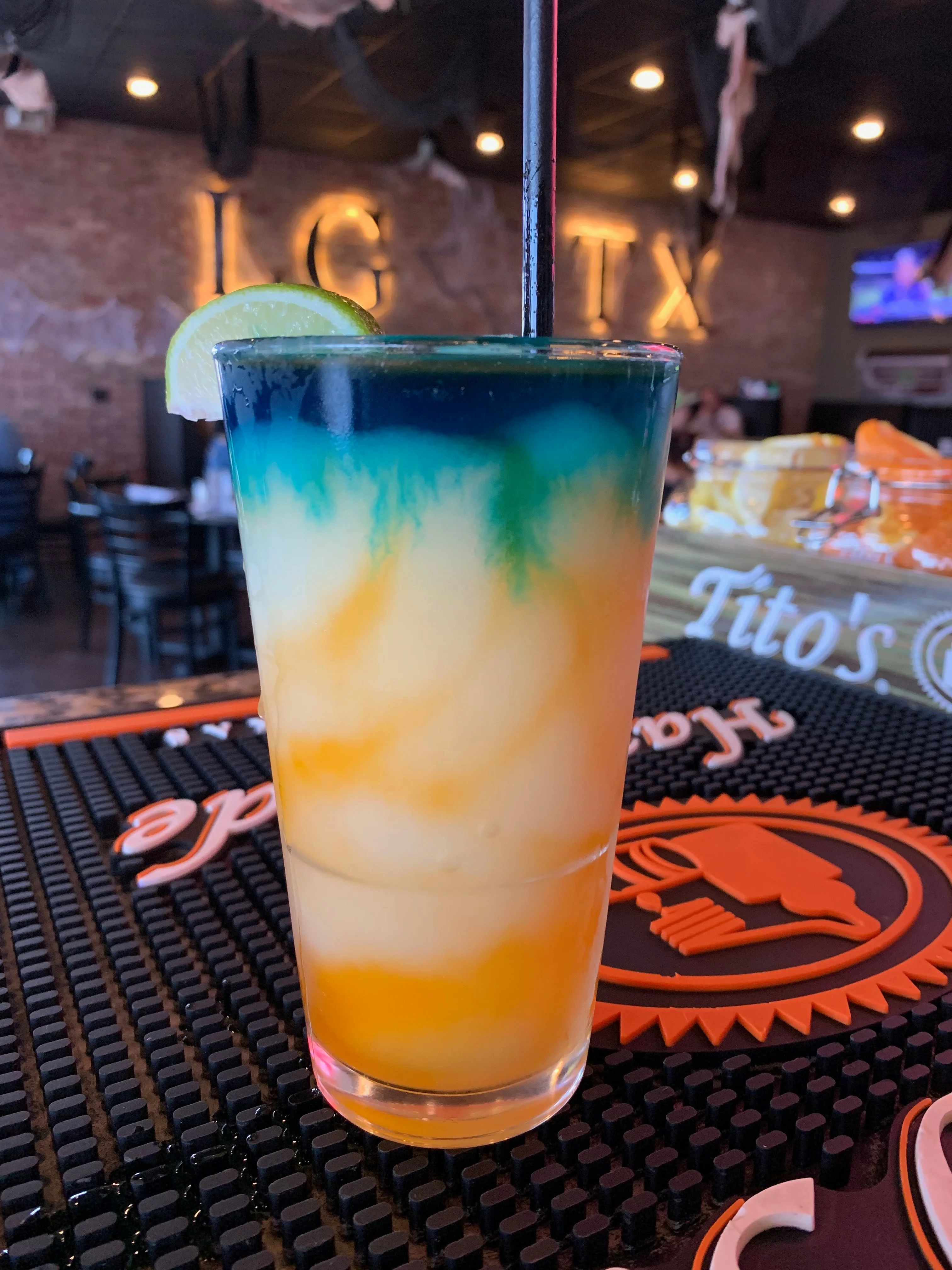 A colorful layered cocktail served with a lime wedge, featuring vibrant blue and orange hues.