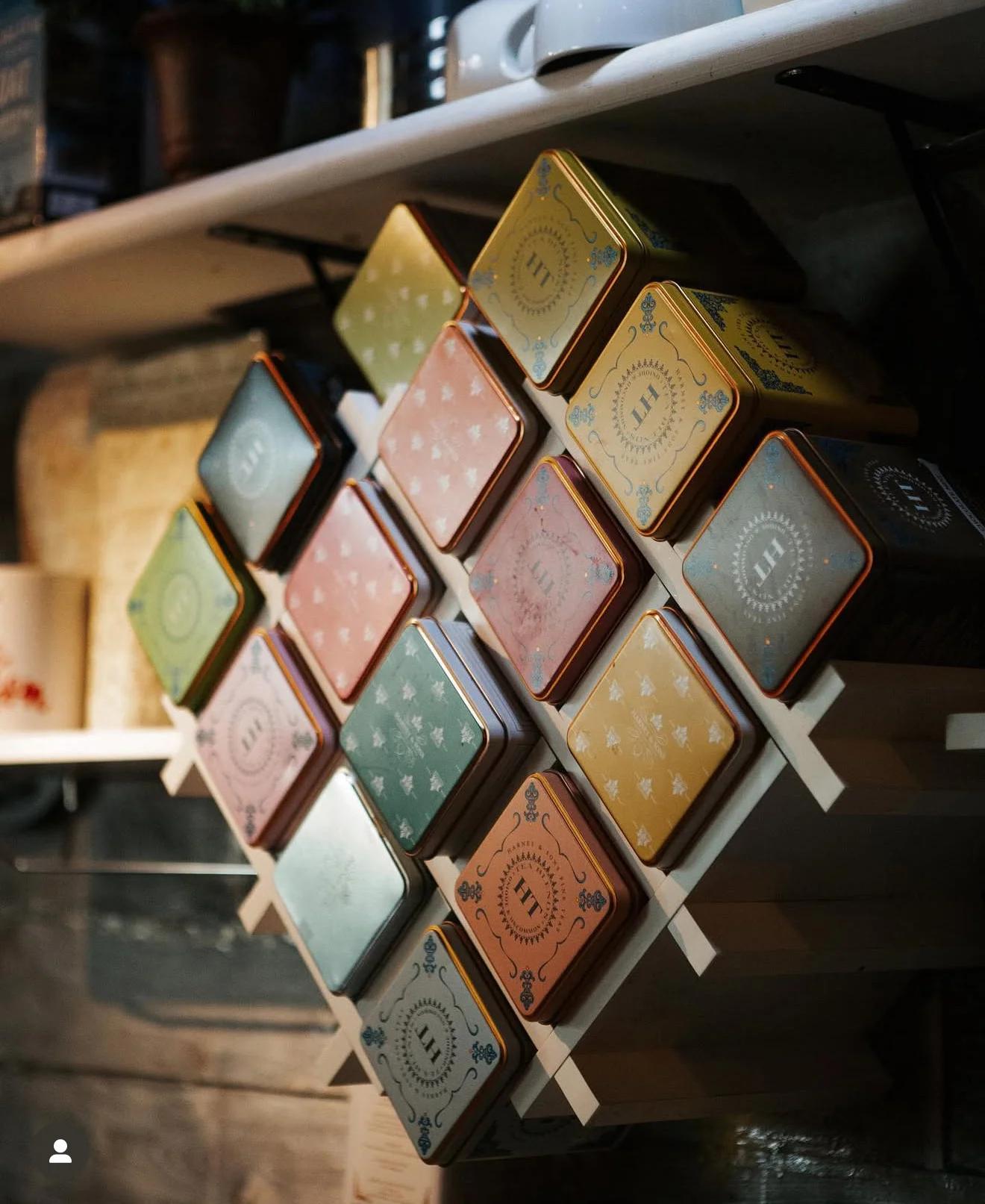 A stylish display of colorful tea tins arranged on a wooden shelf, showcasing various designs and colors.