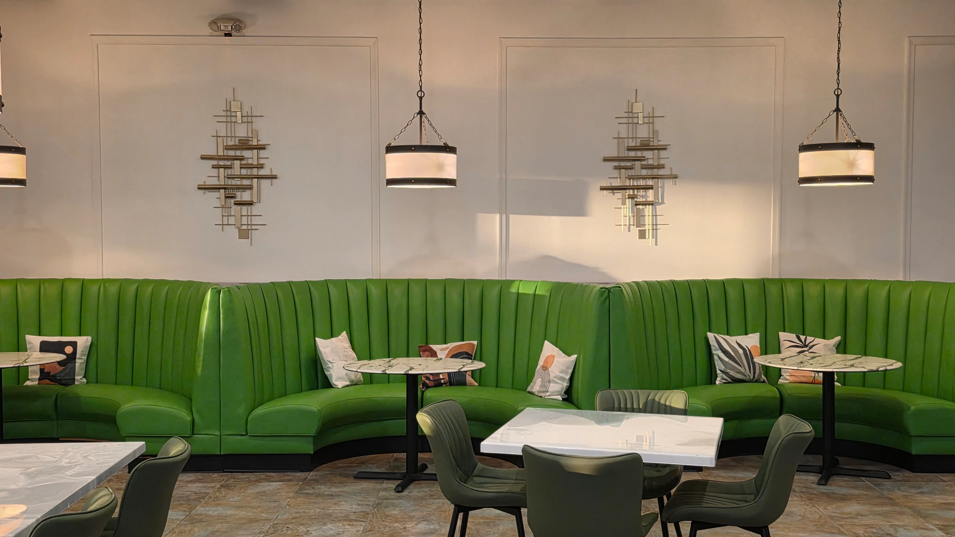 A vibrant green seating area with plush booths, adorned with decorative pillows. A marble-topped table is set within the space, illuminated by stylish overhead lighting.