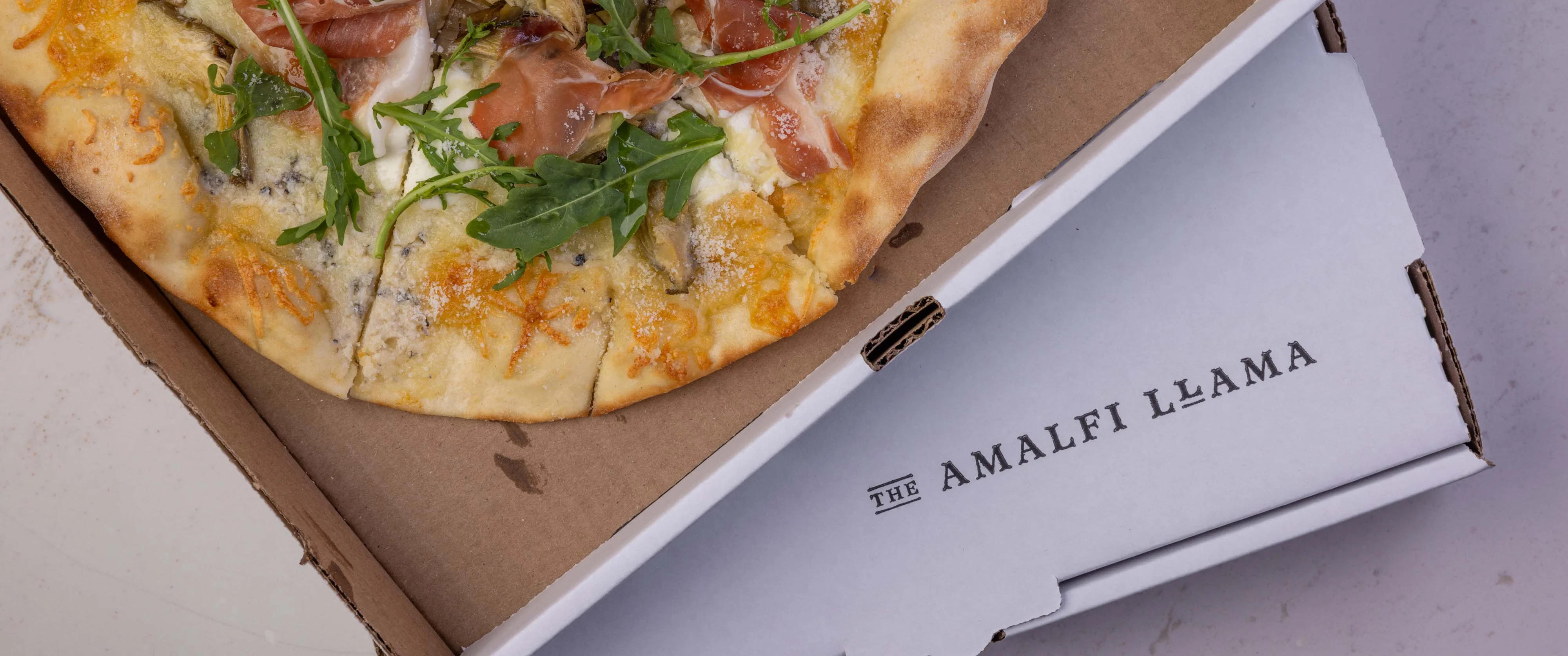 Artisan prosciutto pizza in a takeout box