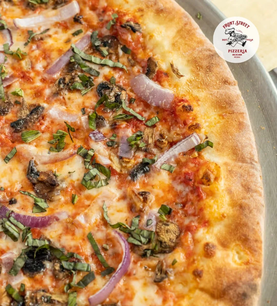 A freshly baked pizza topped with red onions, mushrooms, and basil on a golden crust.