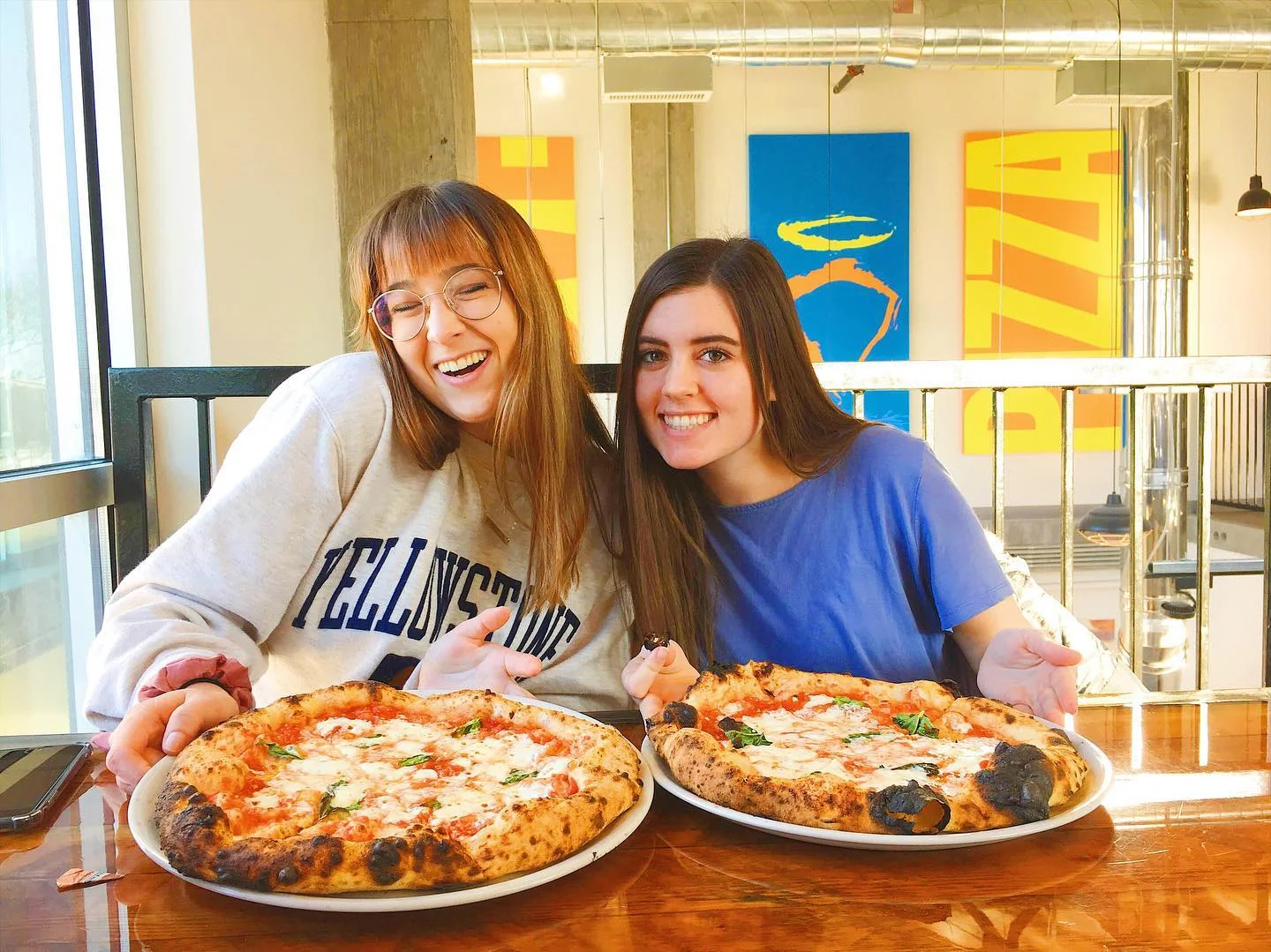 Two friends enjoying Margherita pizzas in a bright restaurant