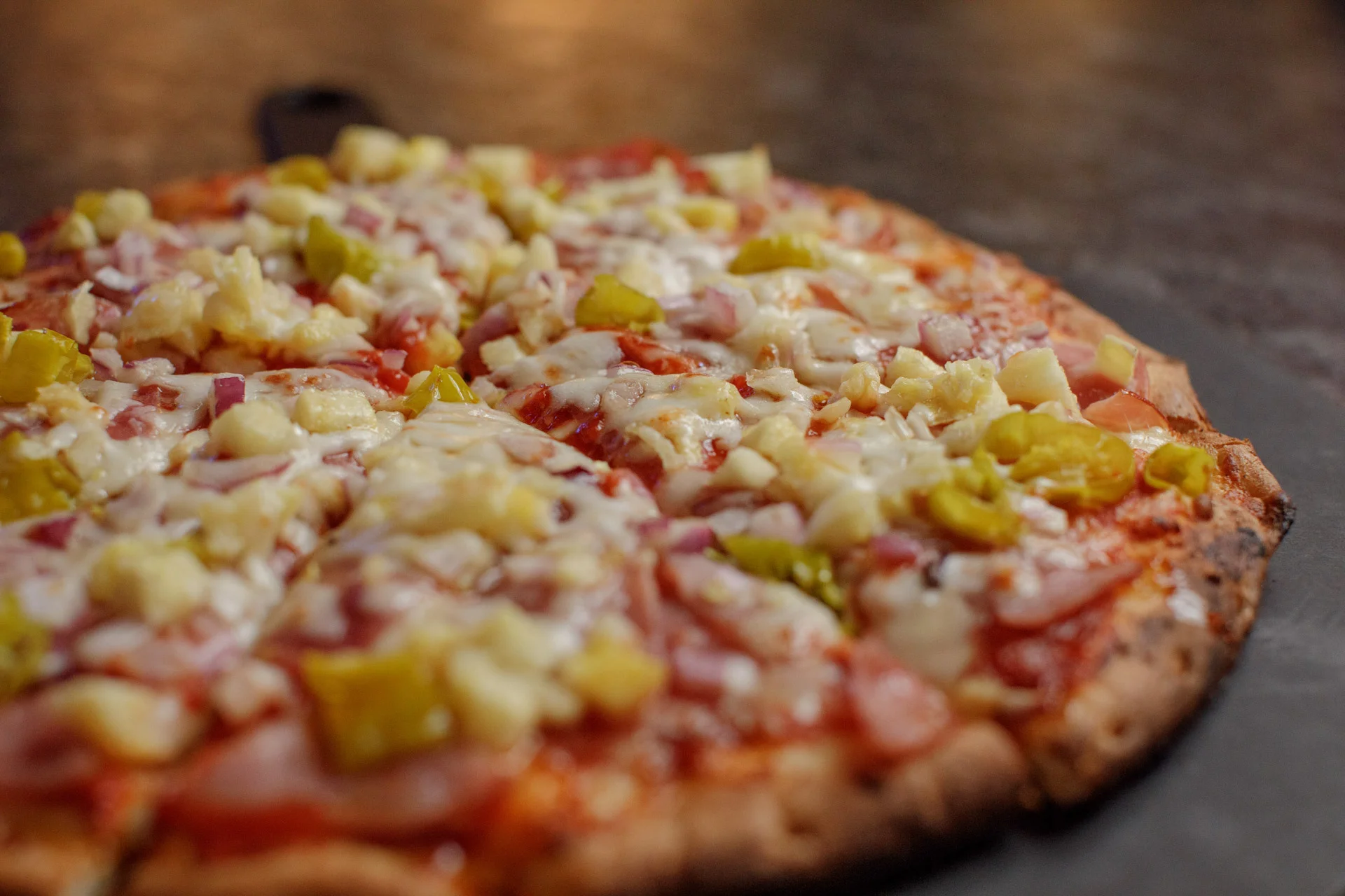 A pizza being cooked in a wood-fired oven, with flames visible and cheese melted over the crust.