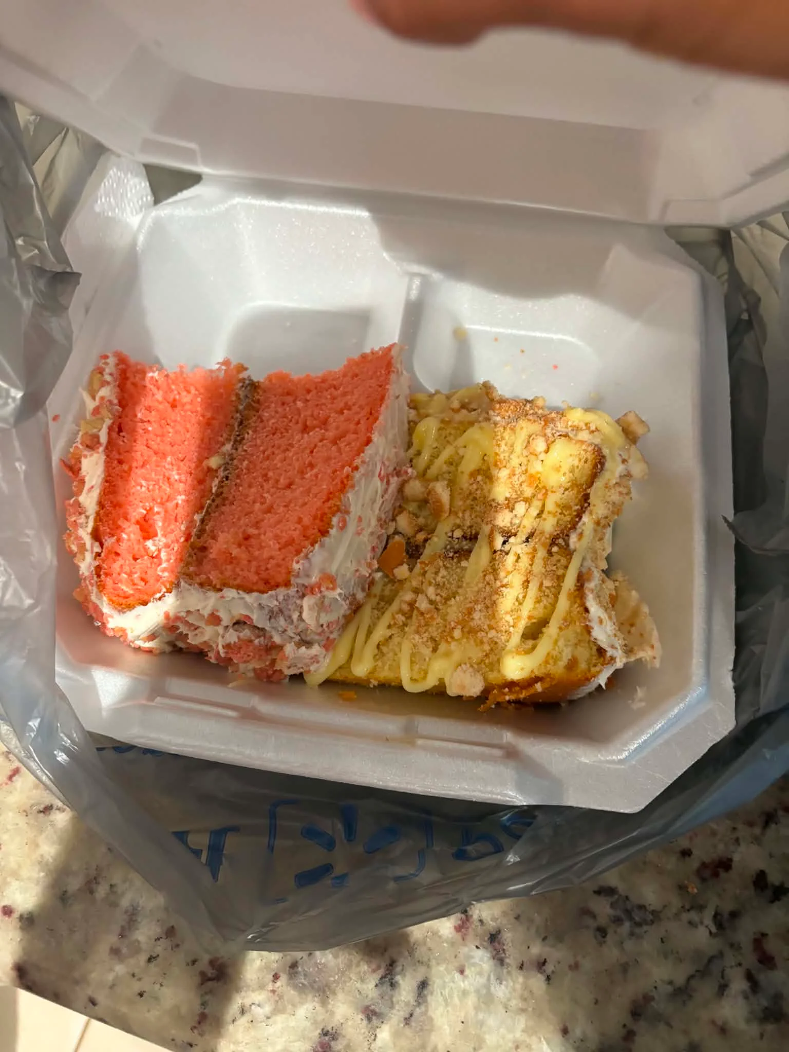 Two slices of cake, one red velvet and the other with a yellow base and icing, placed in a takeout container.