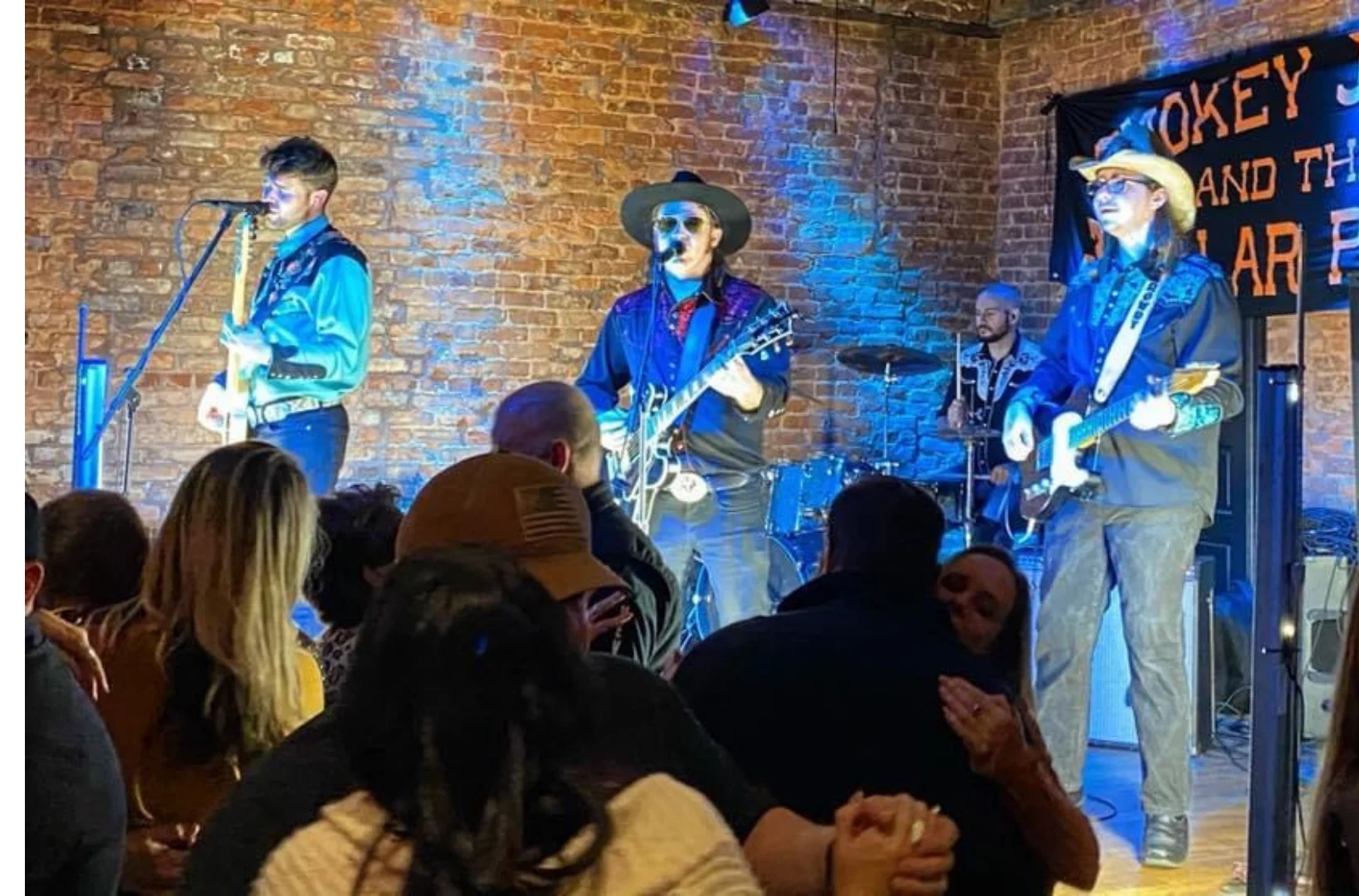 Live band performing on stage in a rustic venue with brick walls
