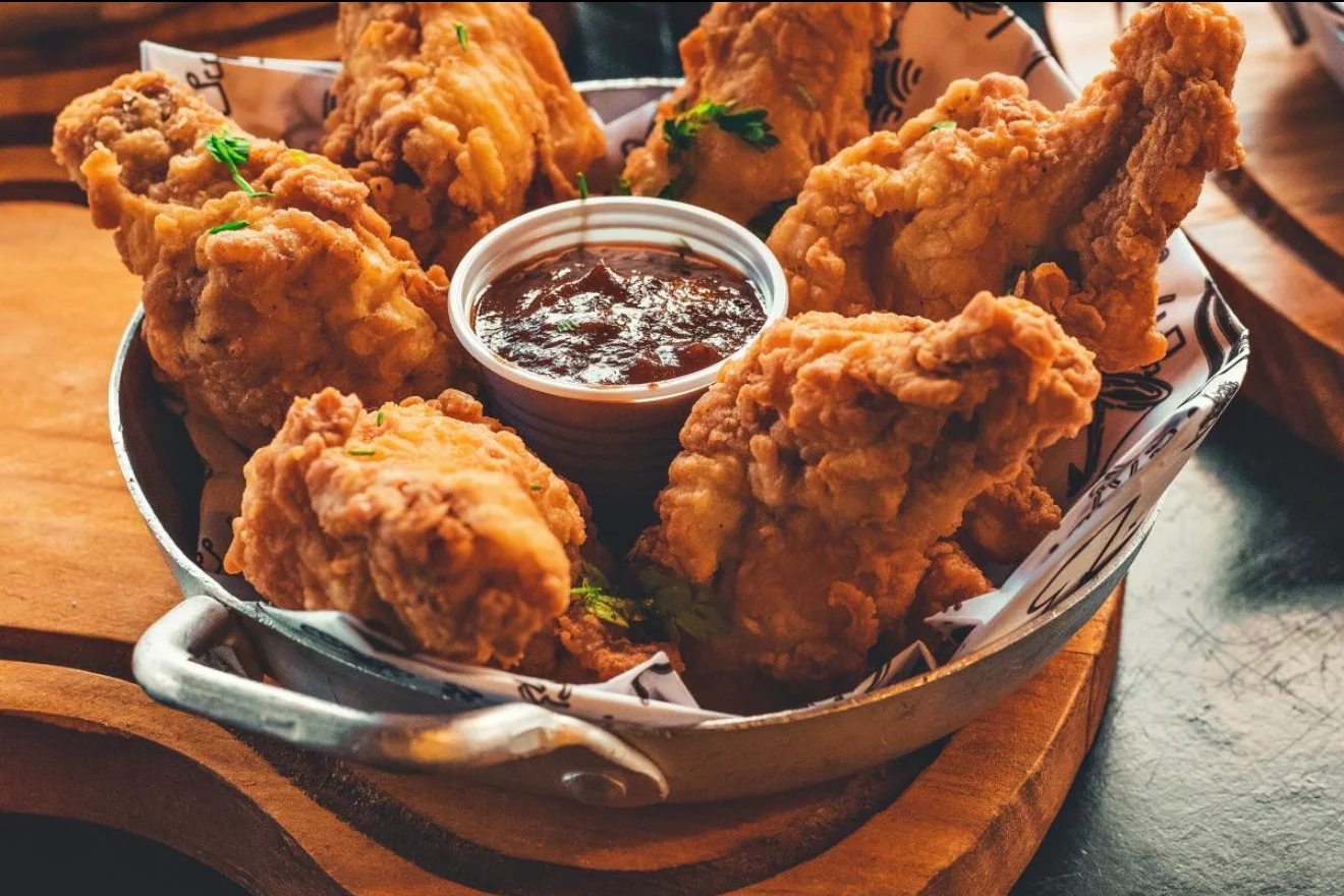 A serving of crispy fried chicken wings served in a metal bowl, accompanied by a small dish of dipping sauce.